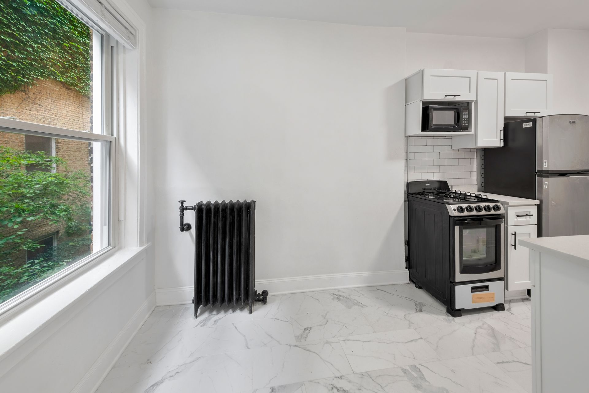 Bright kitchen with white cabinets, stainless steel appliances, window with ivy, and black radiator.