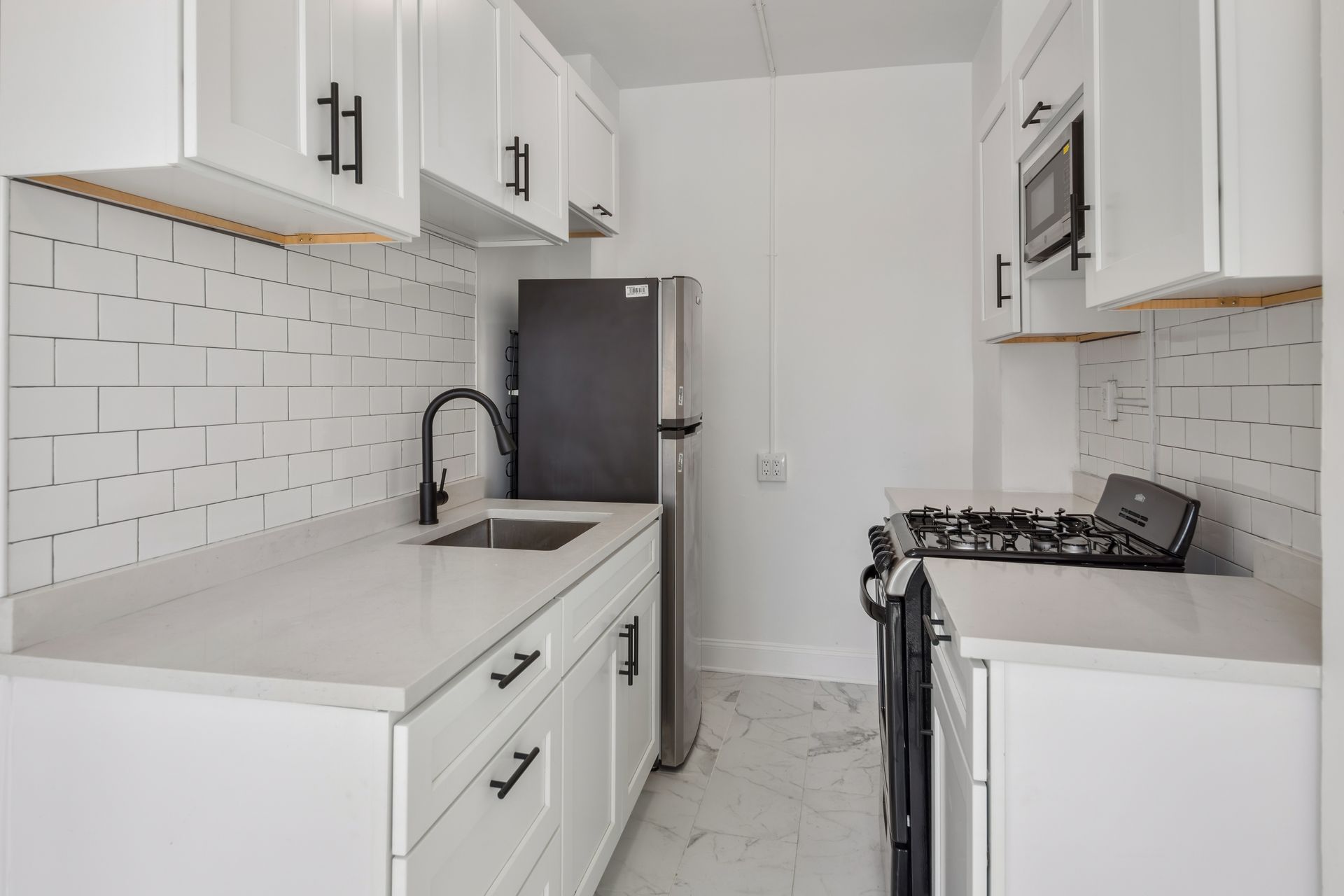 White kitchen with stainless steel appliances, subway tile backsplash, and black hardware.