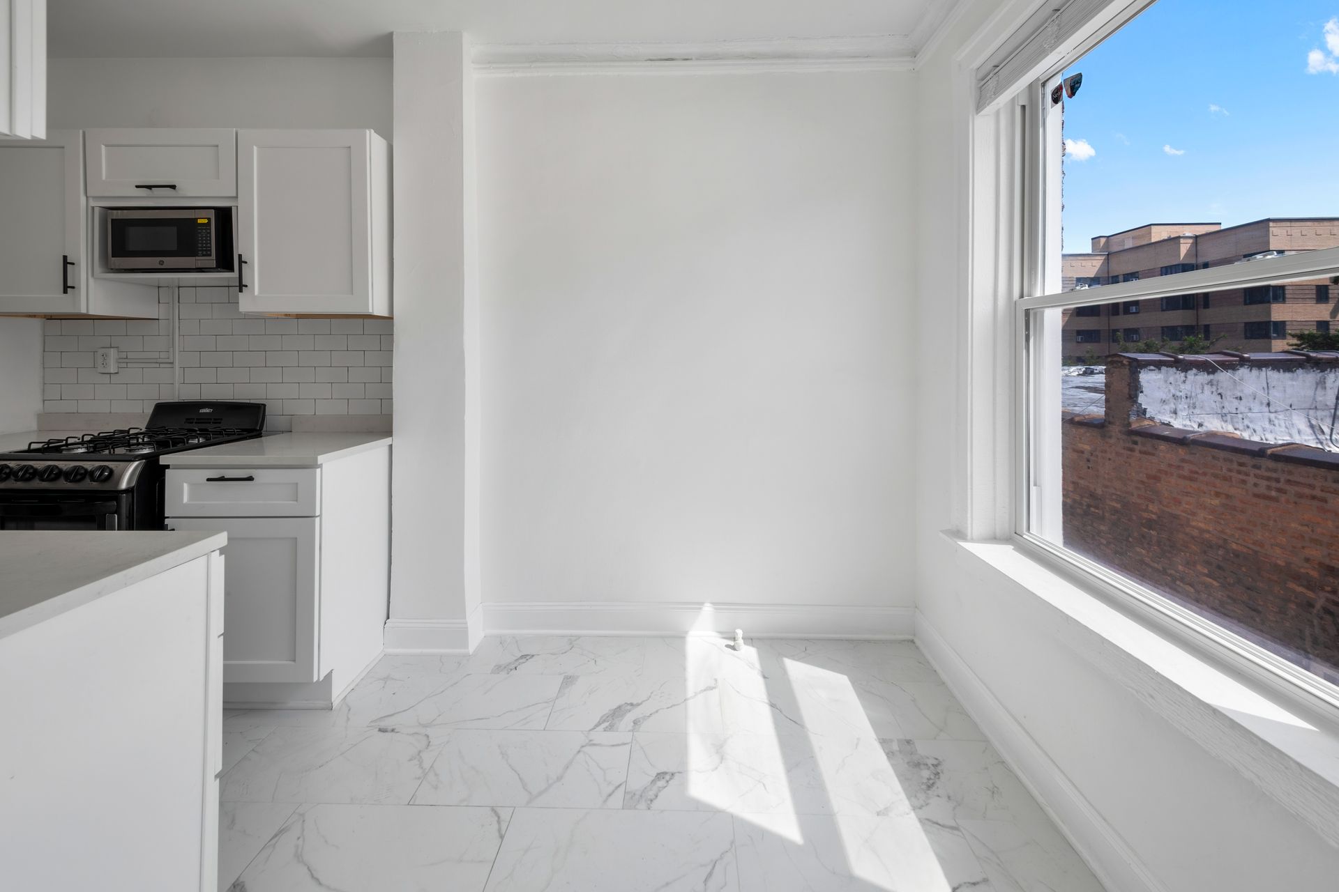 Small white kitchen with window, natural light, and tile floor.