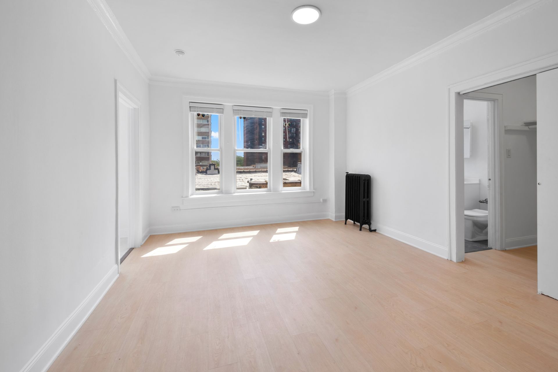 Empty room with hardwood floors, white walls, and a window overlooking a cityscape.