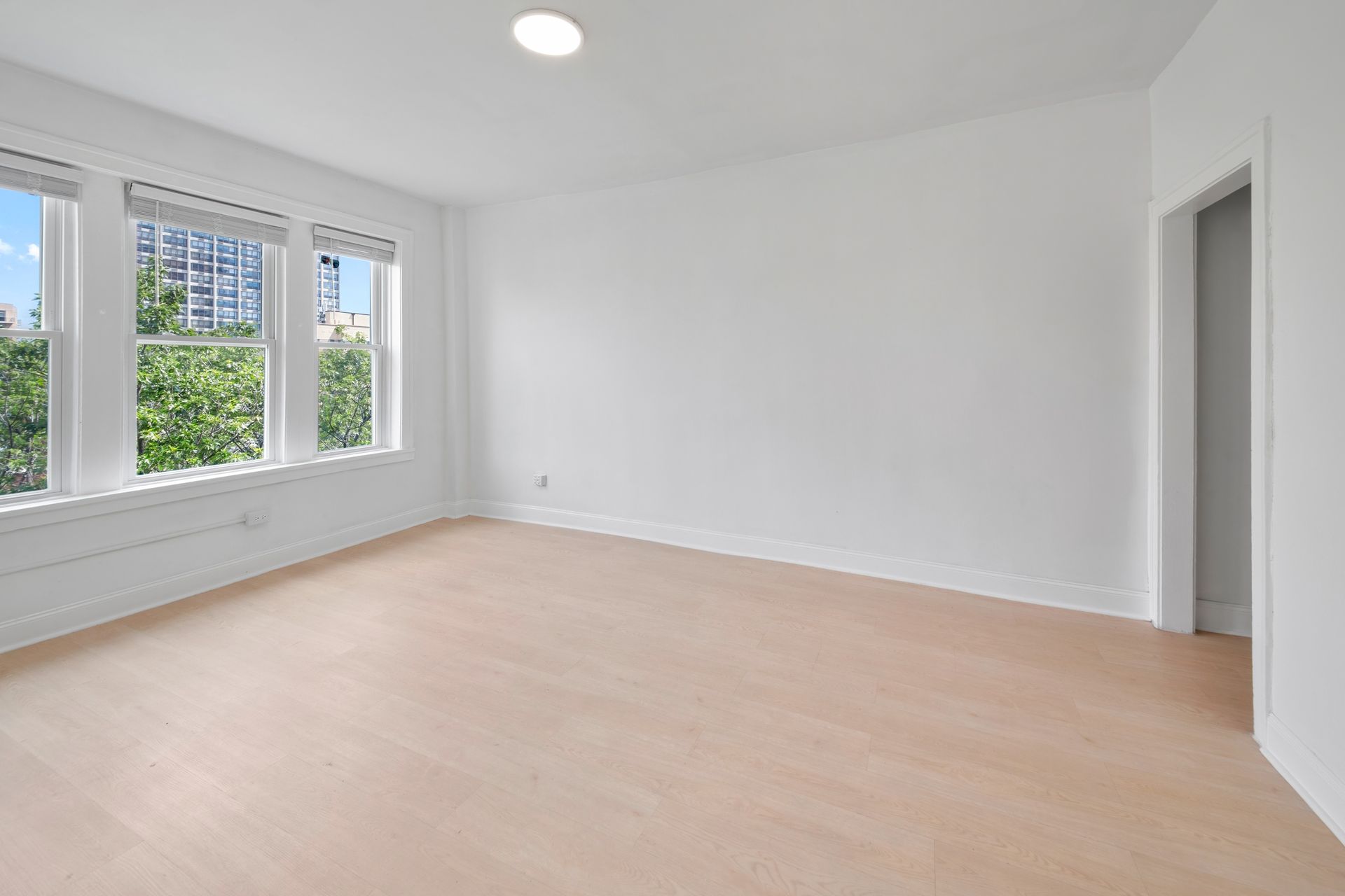 Empty, bright room with wood floors, white walls, and large windows.