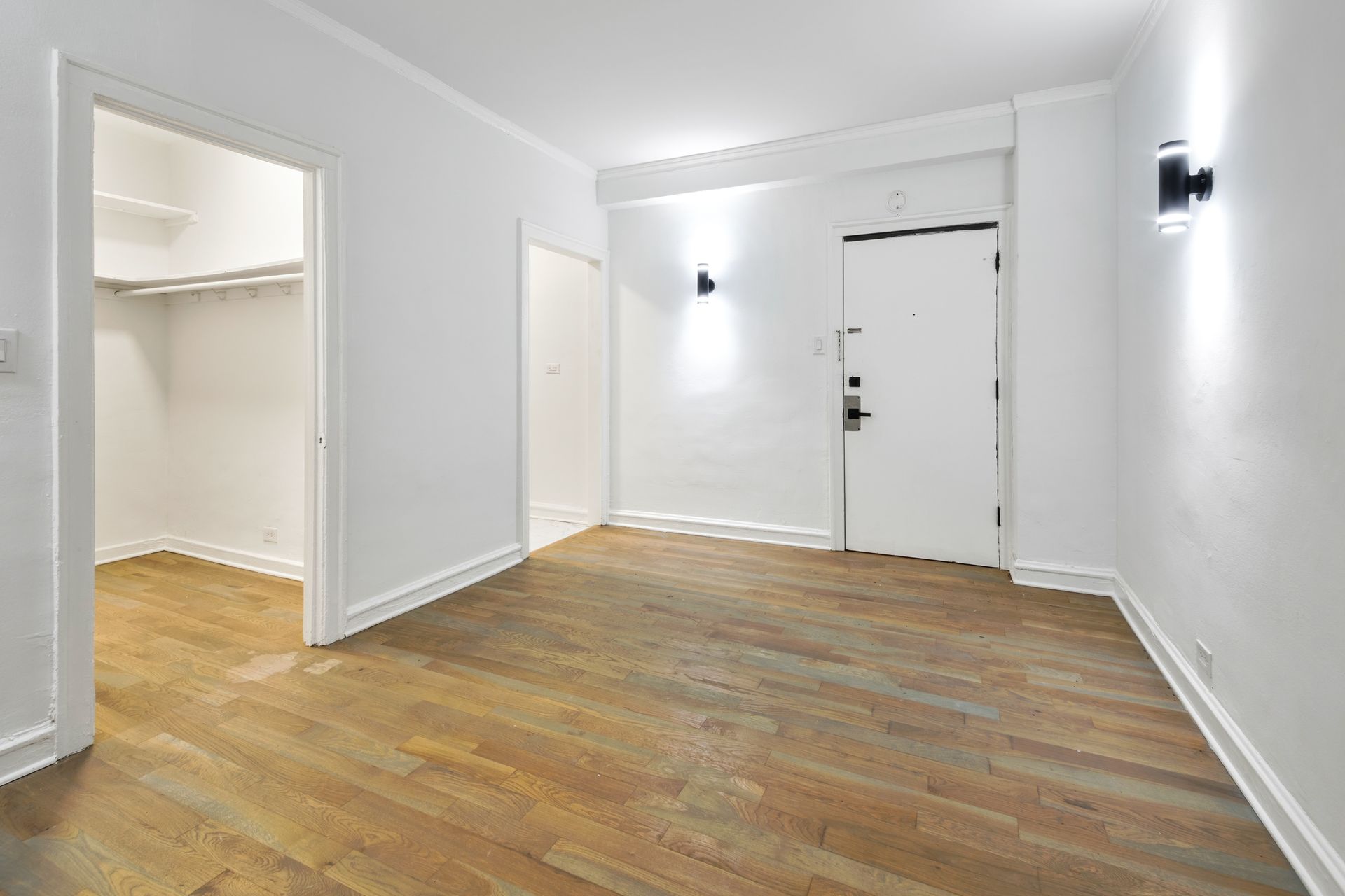 Empty apartment entryway with wooden floor, white walls, and closet.