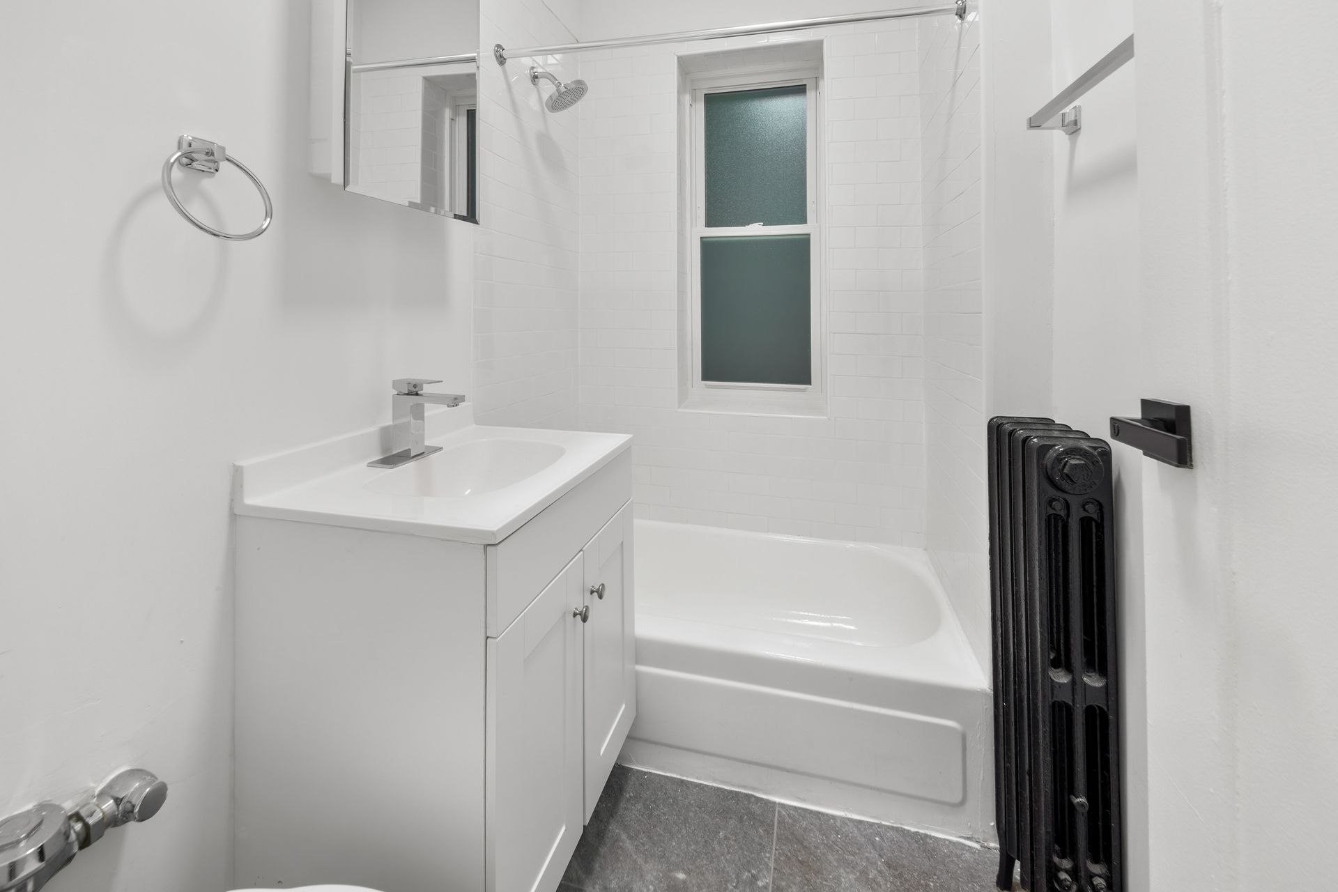 Small, white bathroom with a sink, tub, and black radiator.