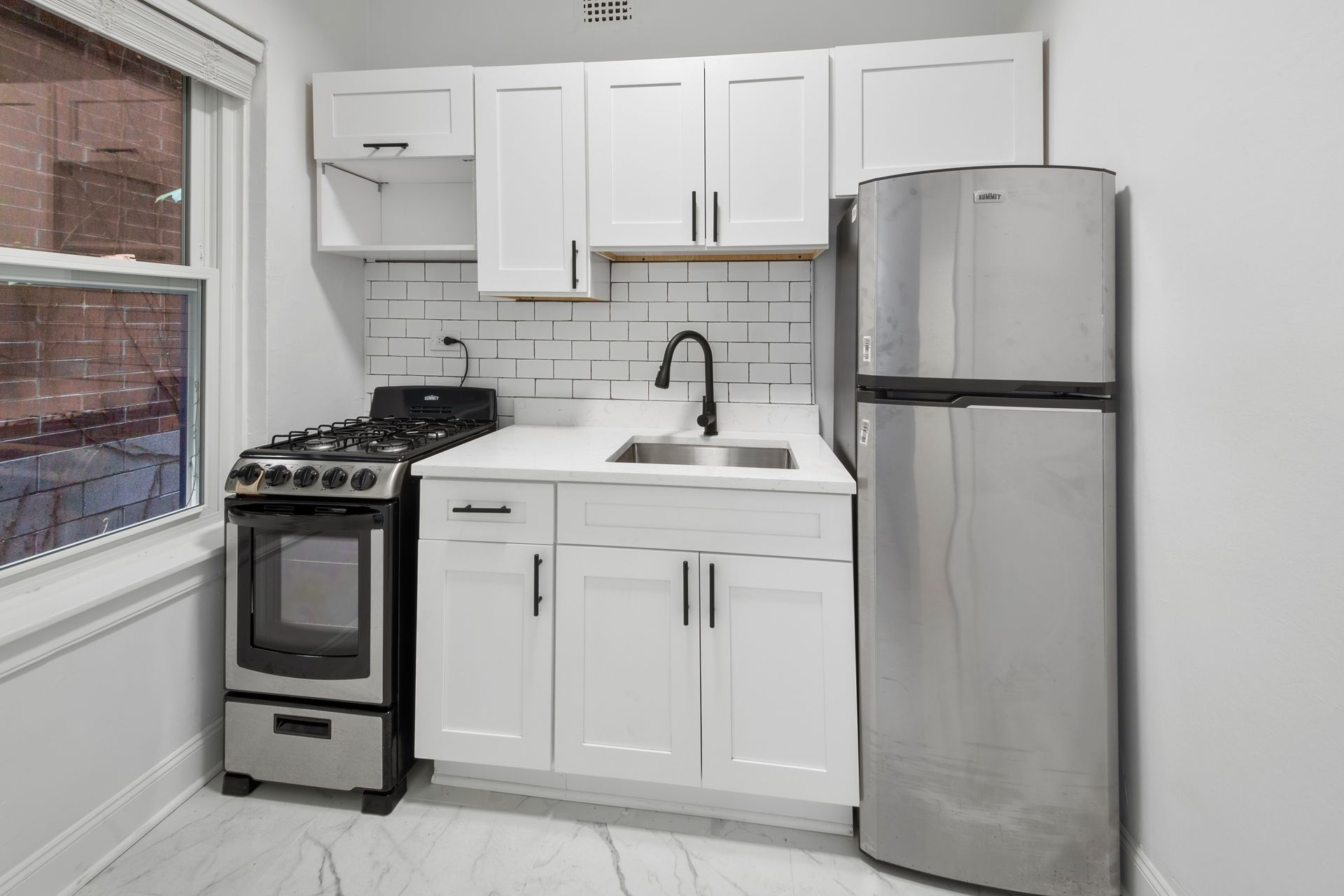 Small kitchen with white cabinets, stainless steel appliances, and white tiled backsplash.