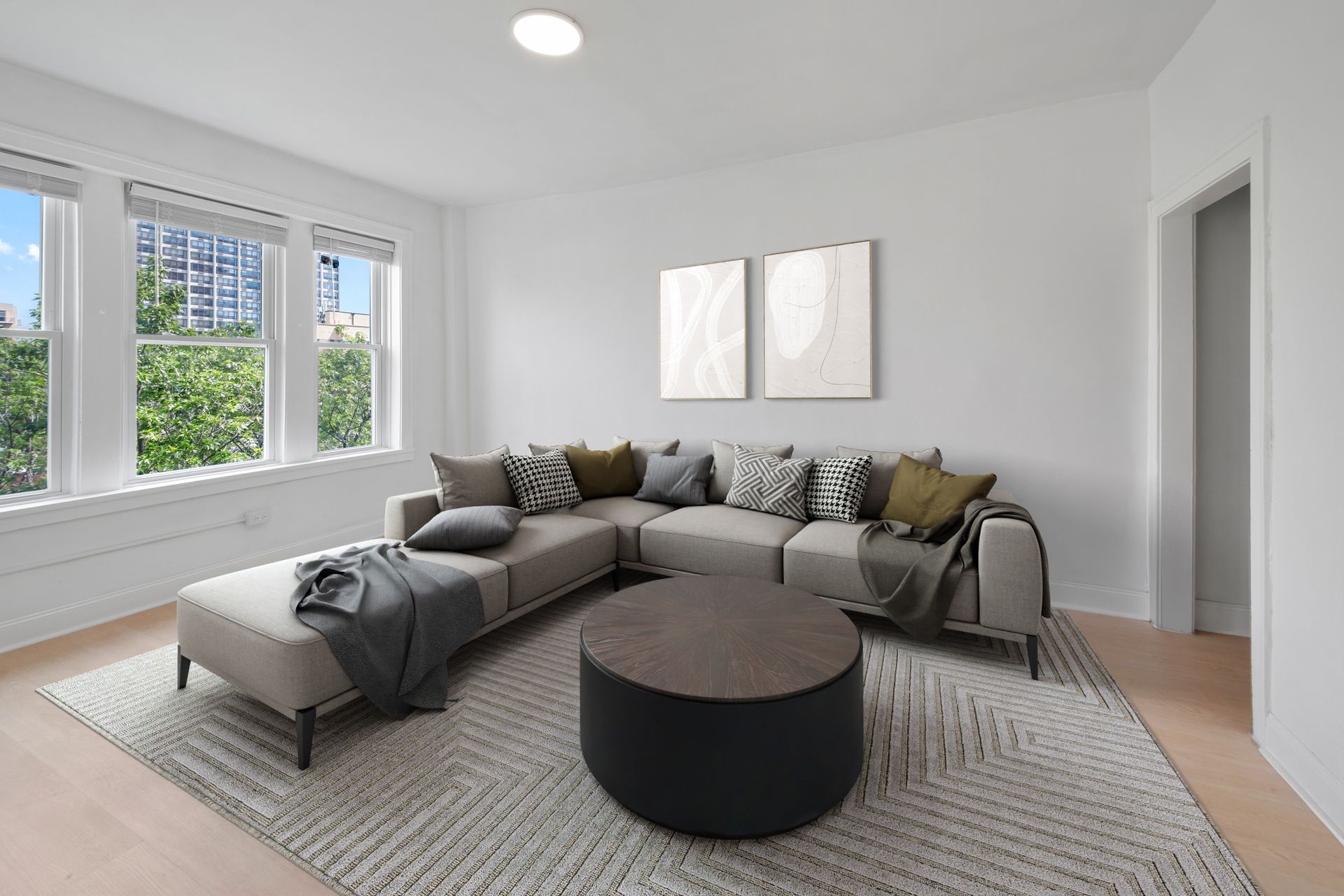 Living room with sectional sofa, large windows, round coffee table, and artwork.
