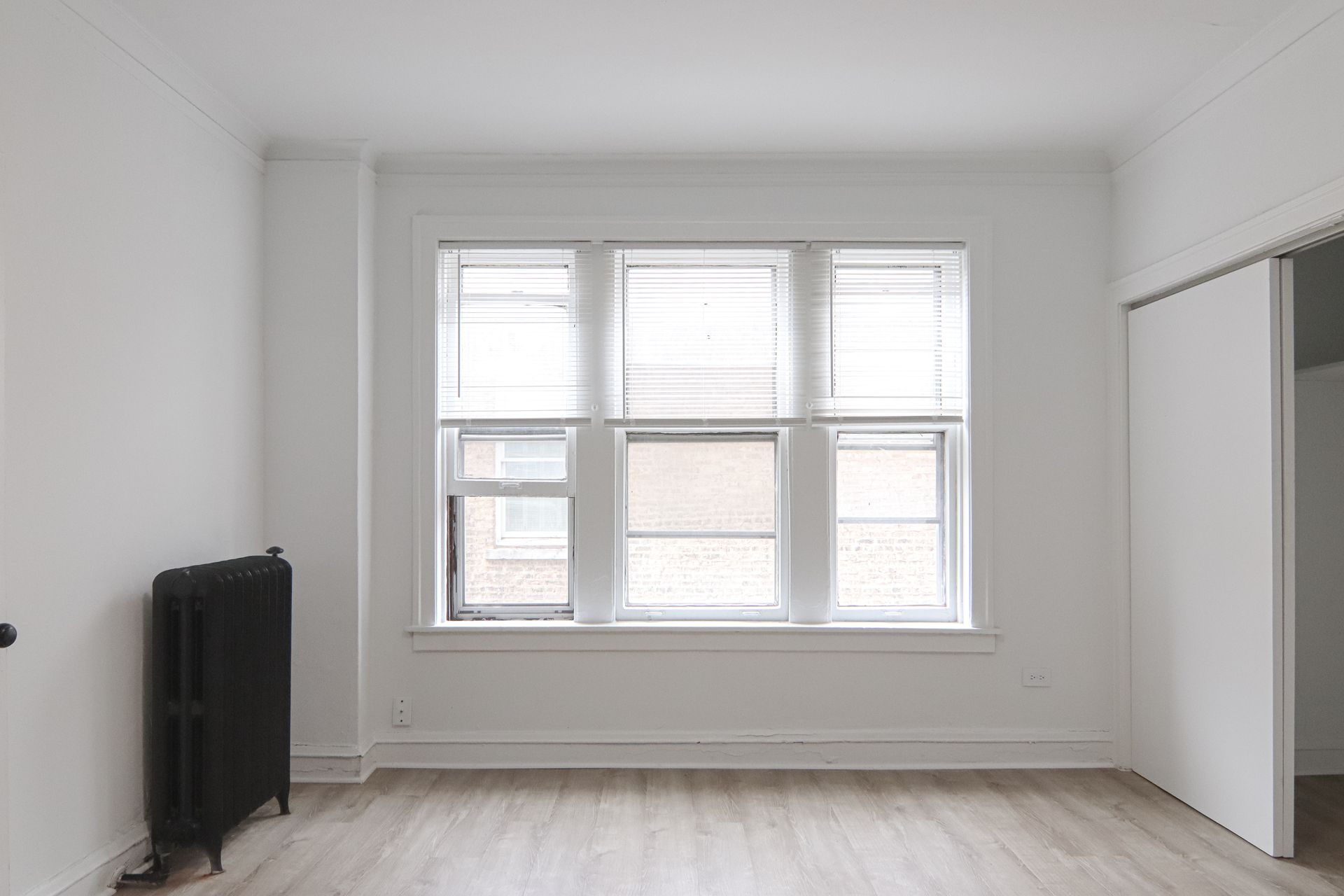 Empty white room with a large window and a black radiator. A closet is on the right.