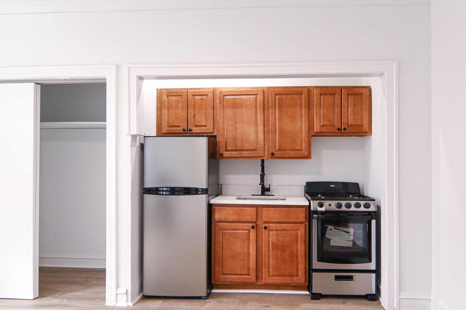 Small kitchen with wood cabinets, stainless steel fridge, and stove. Doorway to closet on left.
