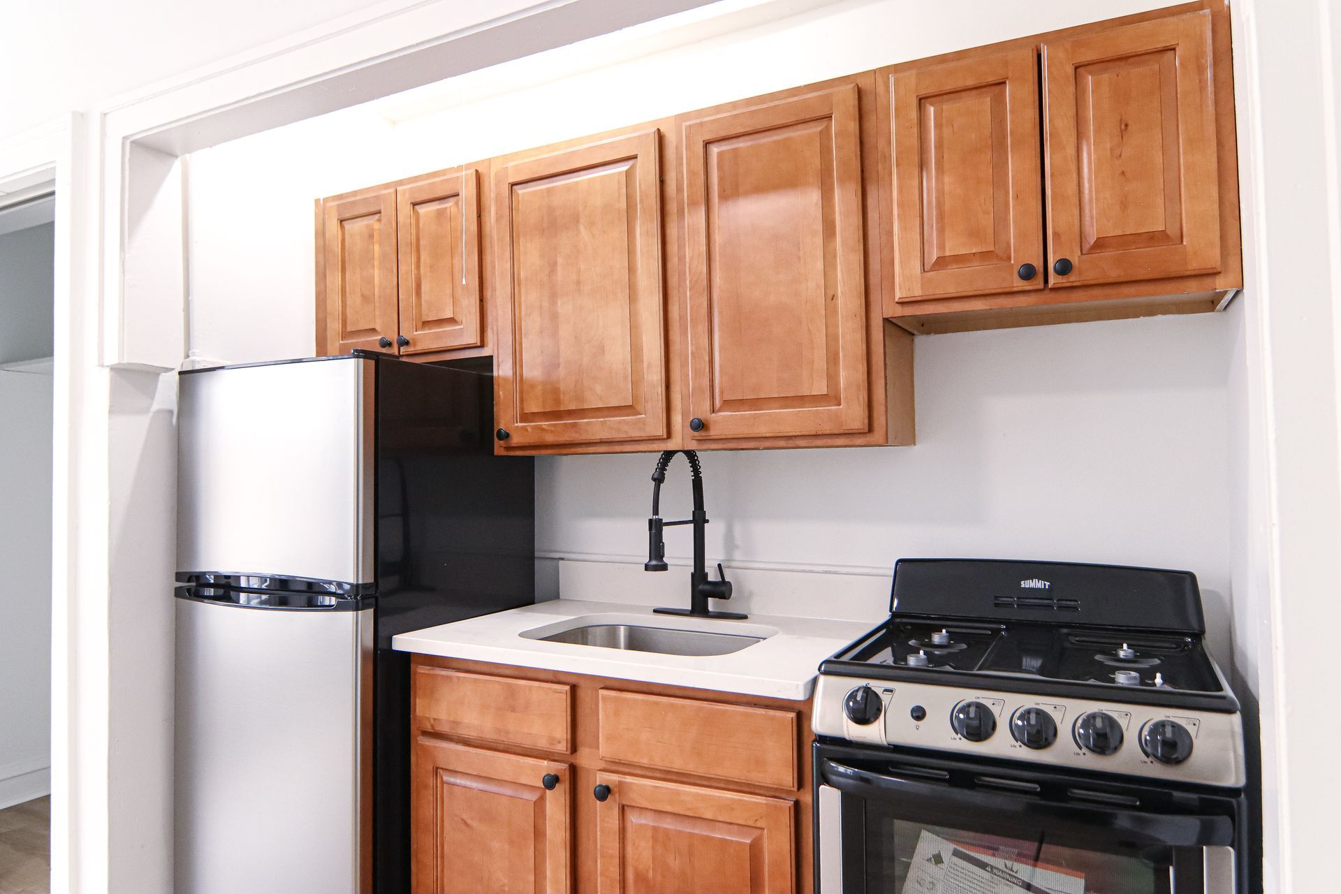 Small kitchen with upper and lower wood cabinets, stainless steel appliances, and black faucet.