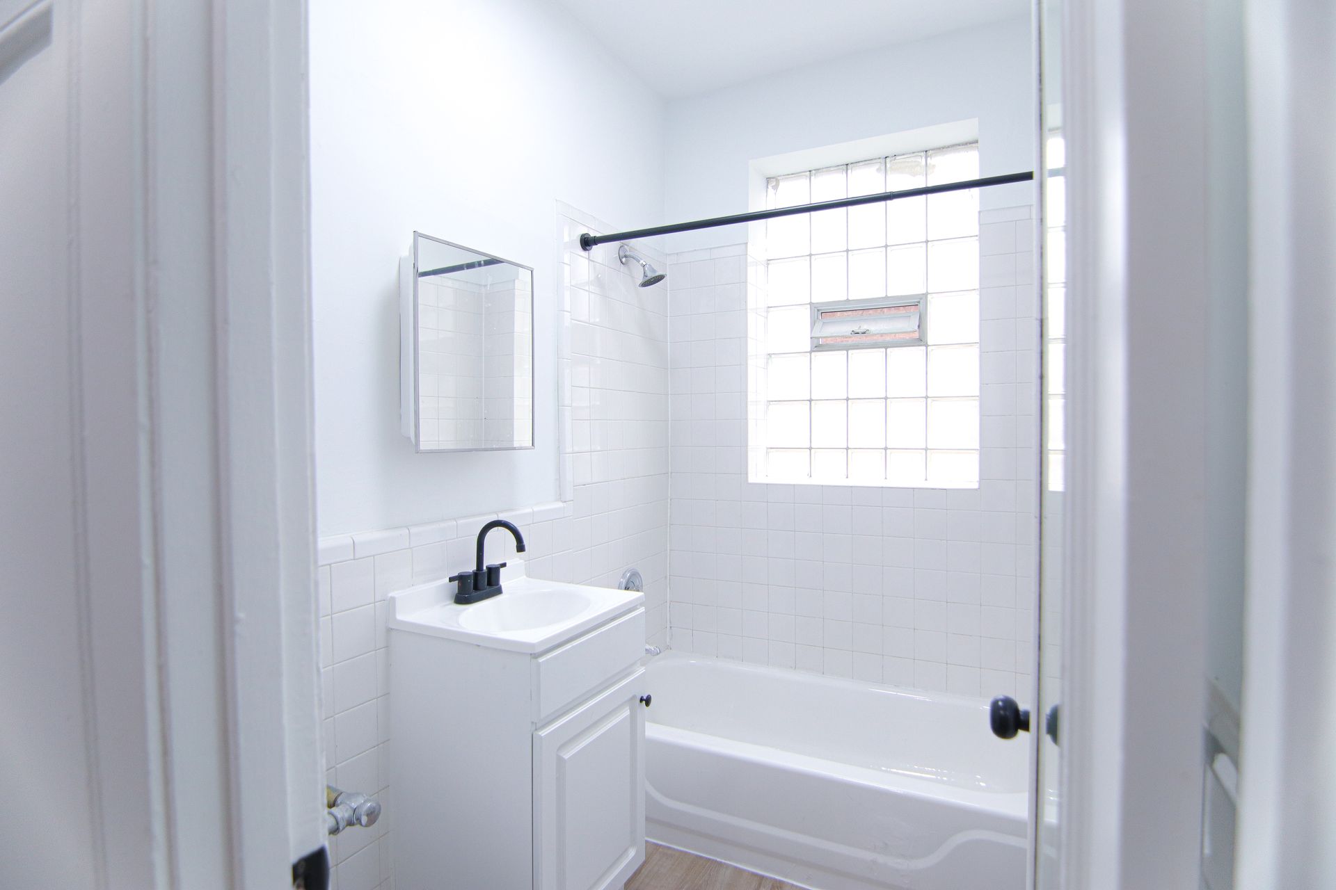 Small, white bathroom with a sink, bathtub, and black fixtures; doorway in the foreground.