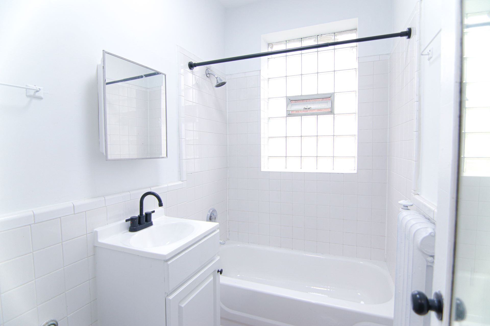 White bathroom with a sink, bathtub, and a glass block window.