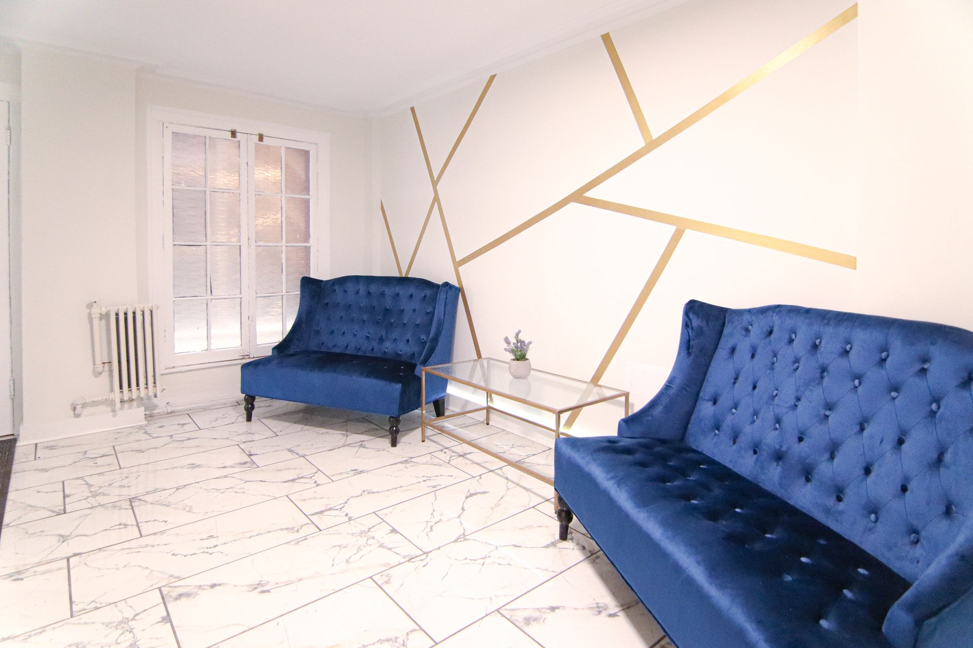 Blue velvet sofas in a white room with gold geometric wall design, marble floor.