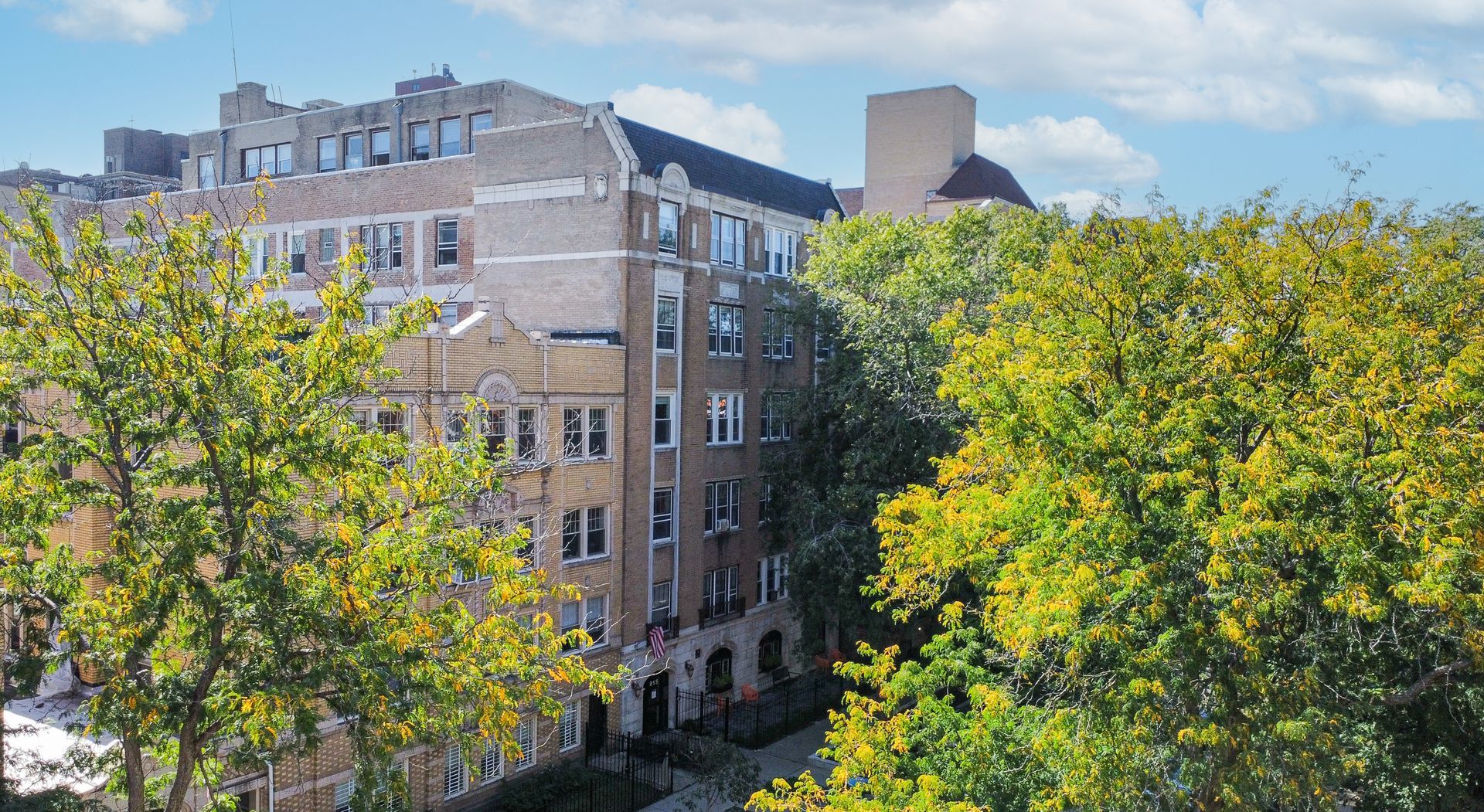Apartment building exterior framed by green and yellow trees on a sunny day.