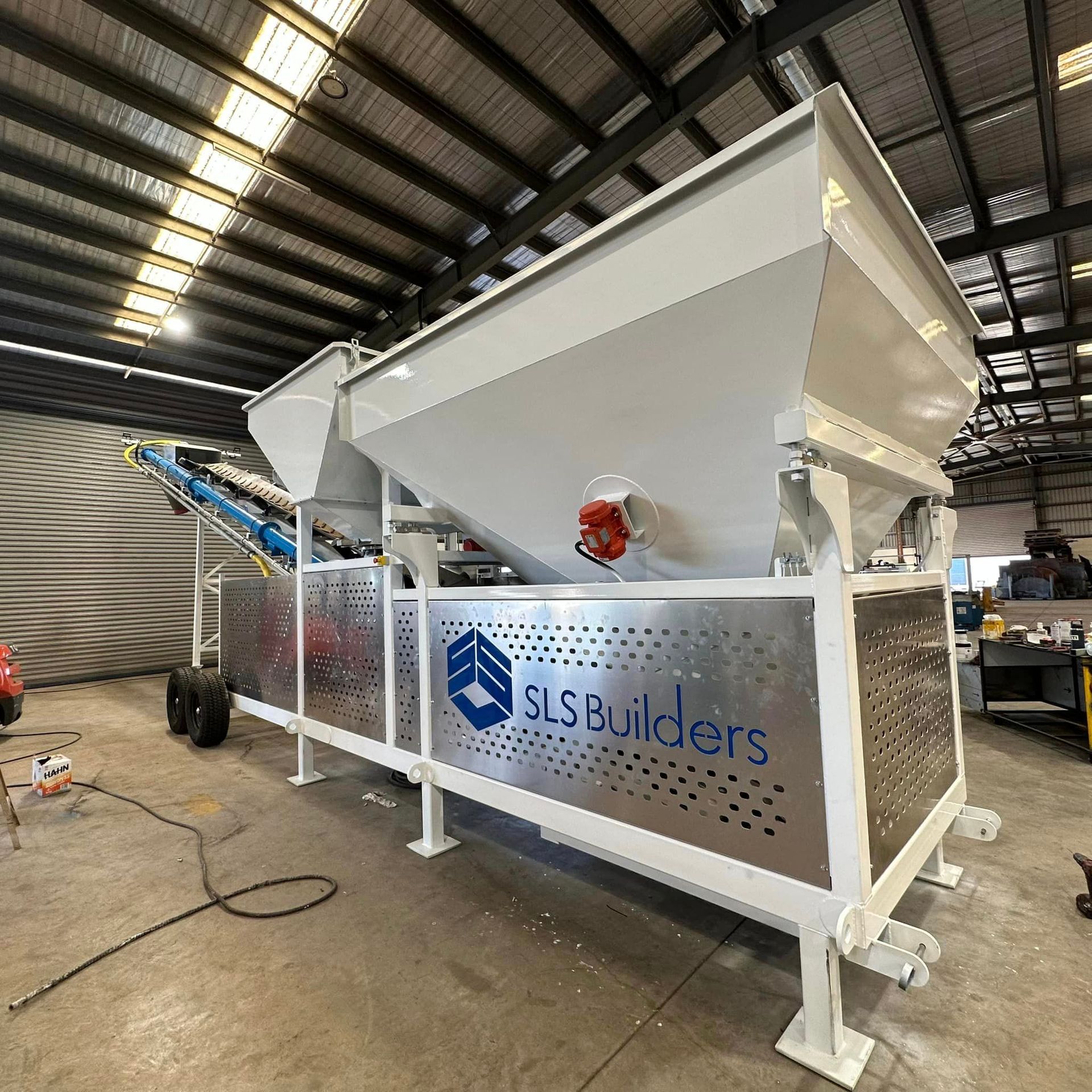 Mobile concrete mixing machine with SLS Builders logo. White and metal with conveyor belt — SLS Builders Pty Ltd in Katherine, NT