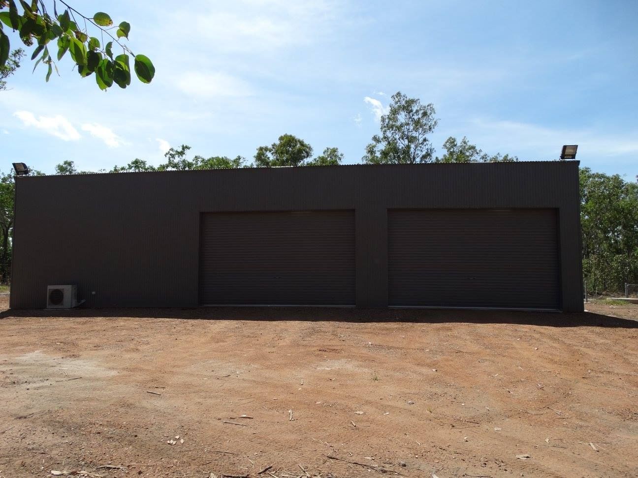 Two-car garage, gray exterior, roll-up doors, located on a dirt lot, with blue sky background — SLS Builders Pty Ltd in Humpty Doo, NT
