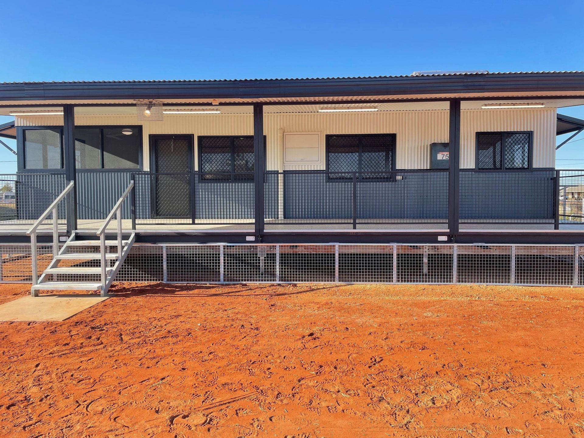 A white building with a black railing and steps on red dirt under a blue sky — SLS Builders Pty Ltd in Alice Springs, NT