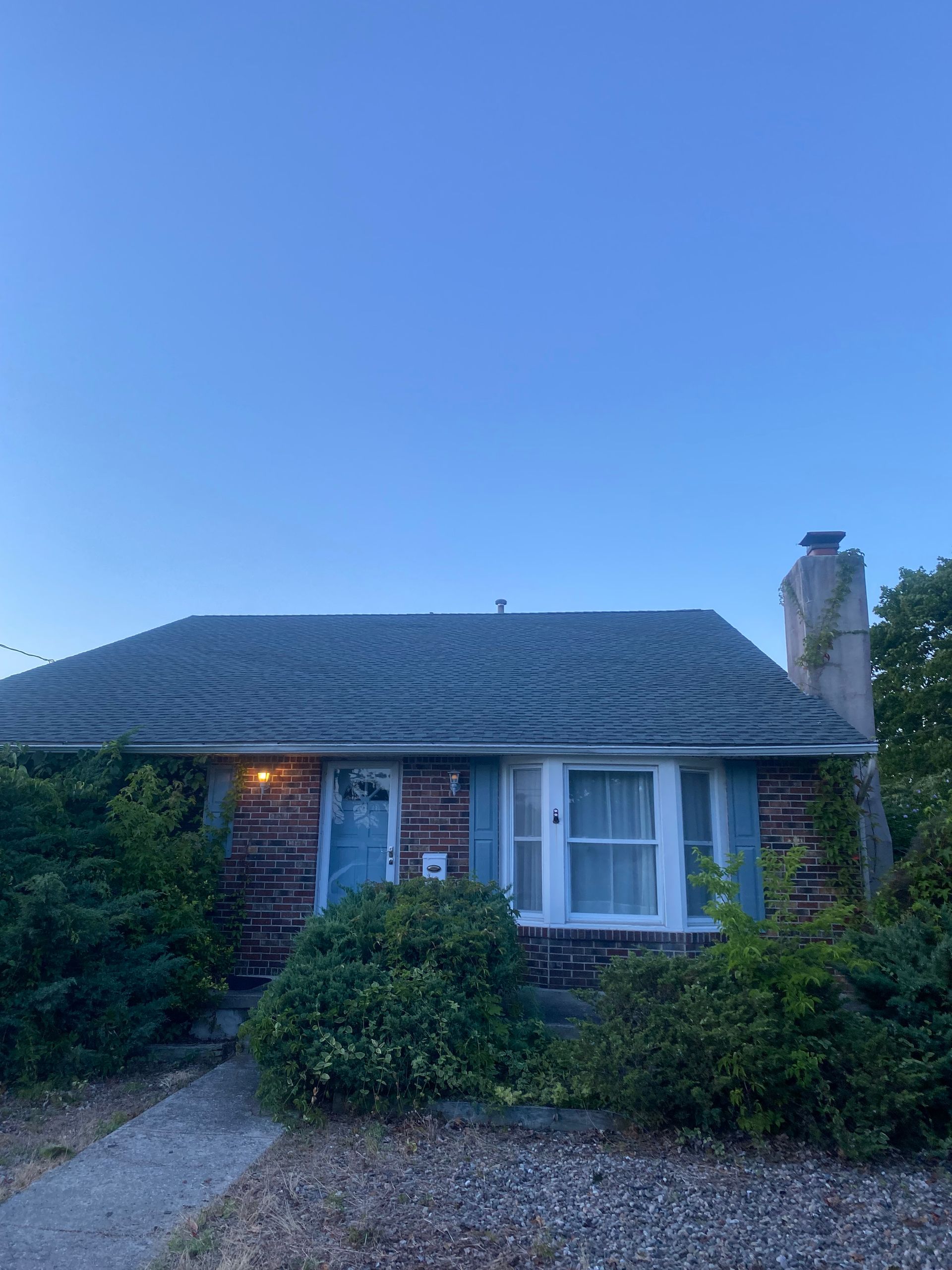 A small brick house with a gray roof and blue shutters.