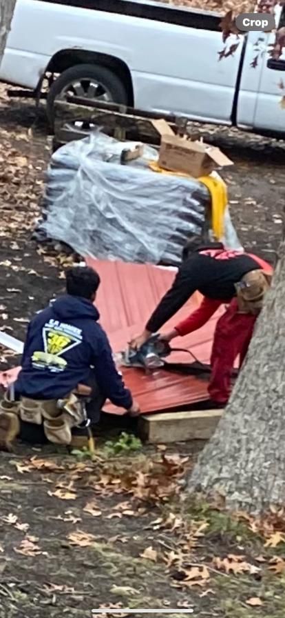A group of men are working on a red roof in front of a white truck.