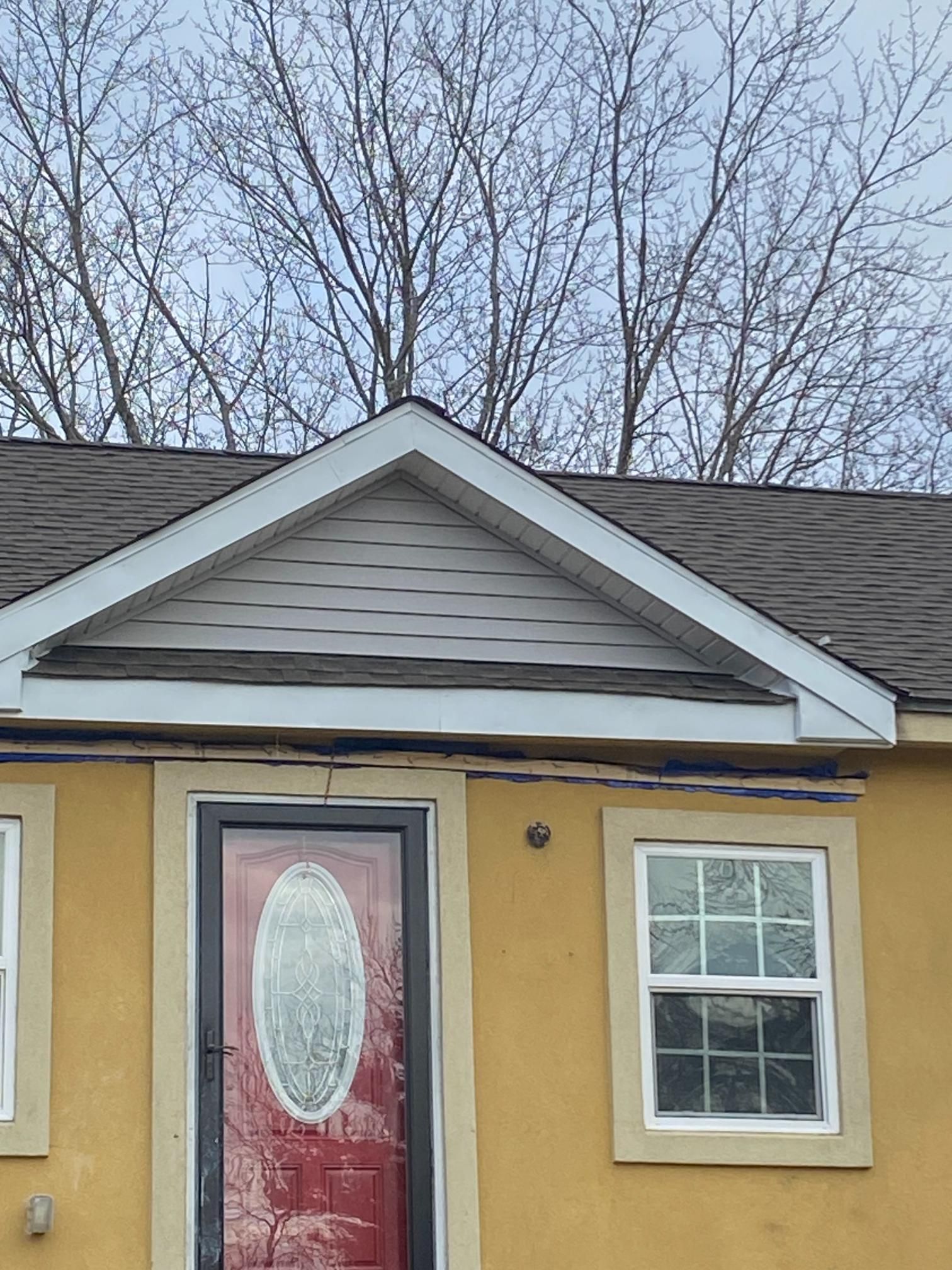 A yellow house with a red door and two windows.