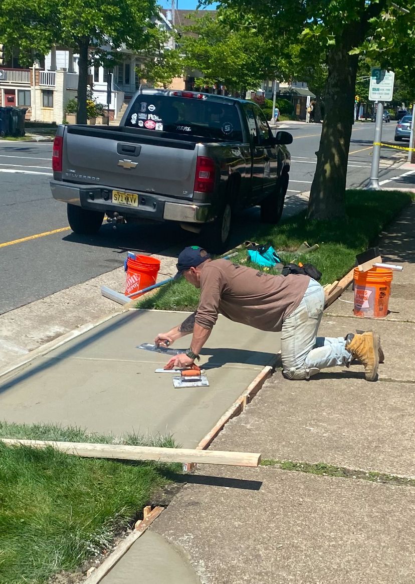 A man is kneeling down on a sidewalk in front of a truck.