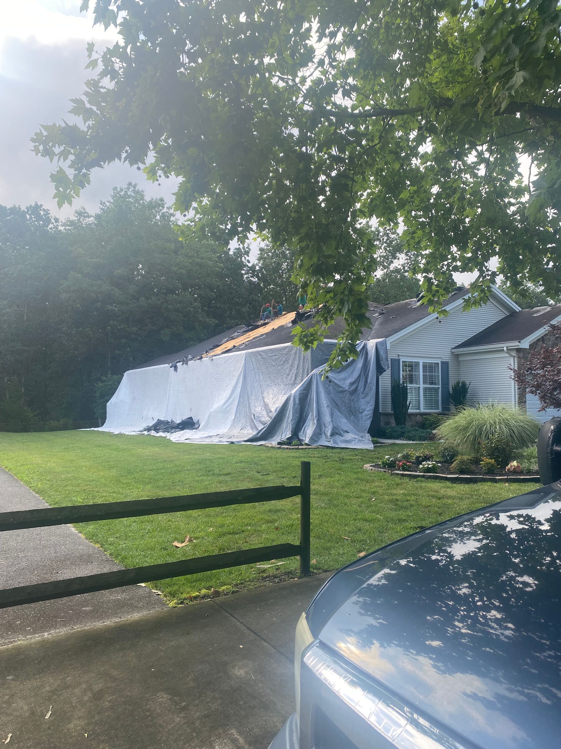 A car is parked in front of a house with a tarp on the roof