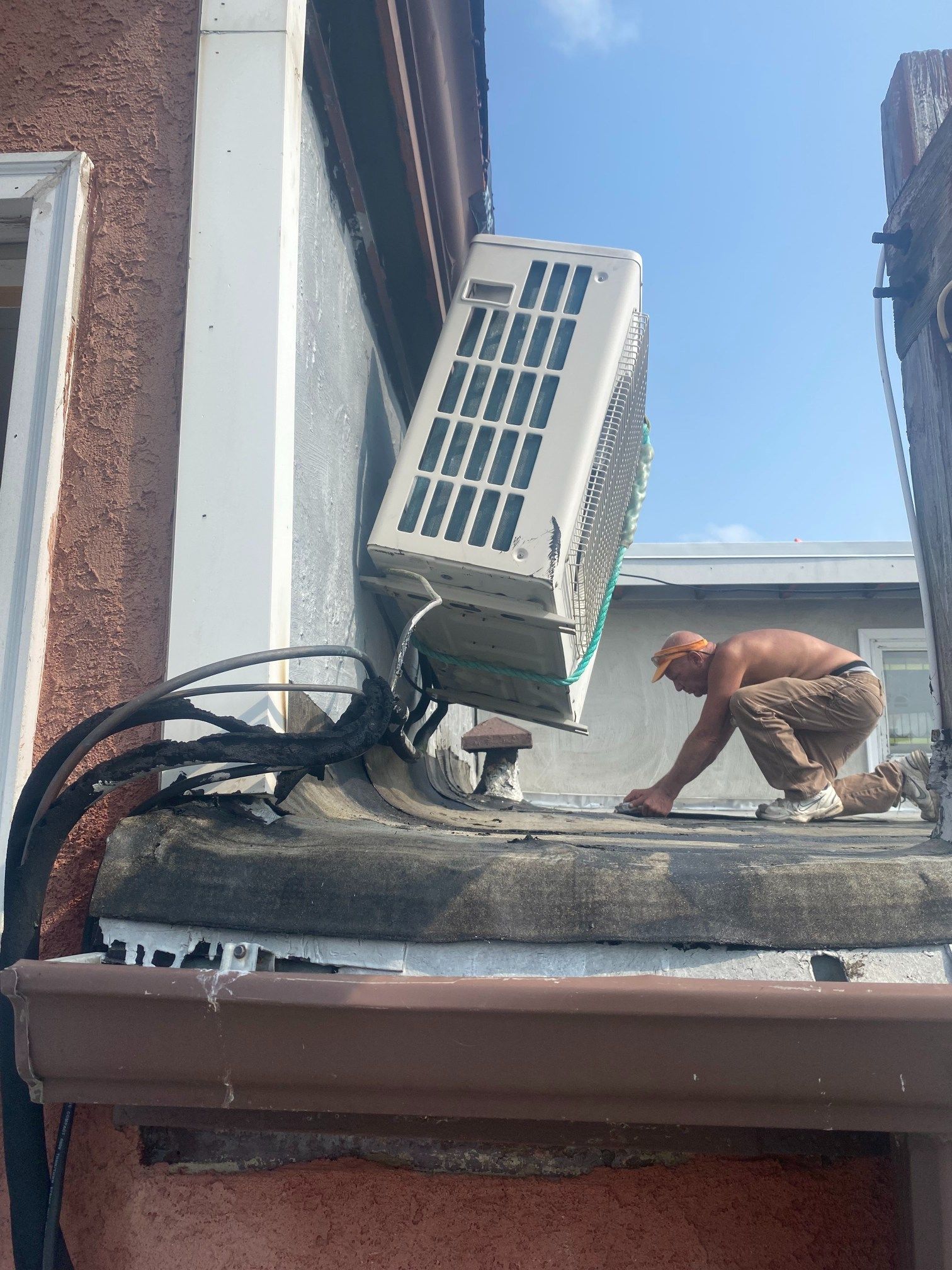 A shirtless person works on a rooftop near an air conditioner unit; the sky is blue.