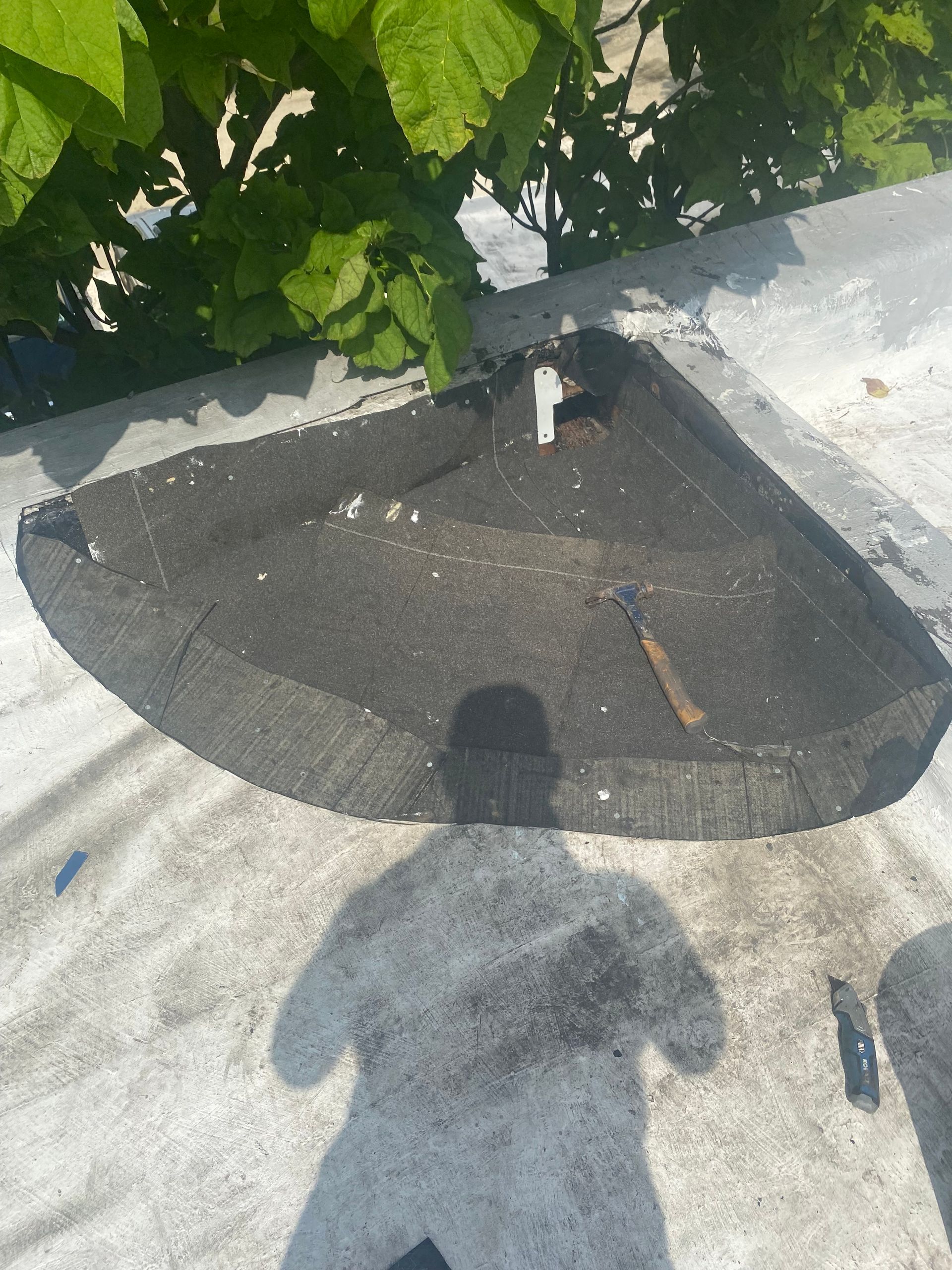 Black roofing repair with tools on a flat roof, shadow of a person above.
