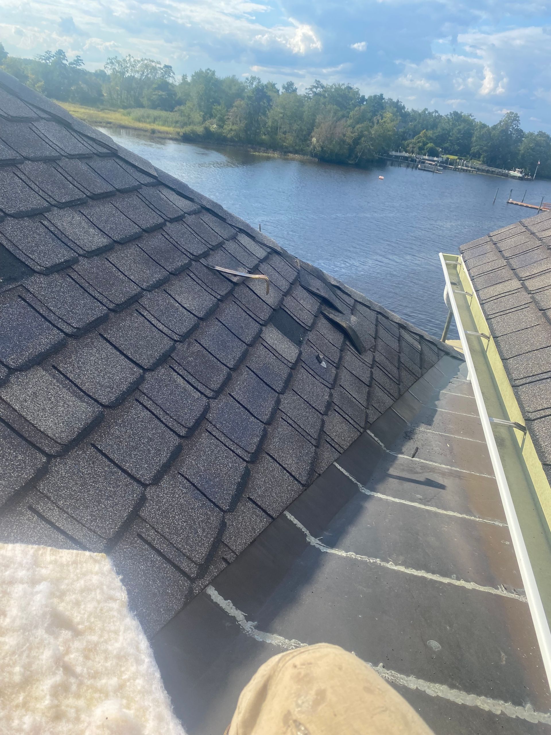 Damaged roof shingles near water under a partly cloudy sky.