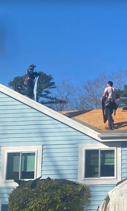 Two workers replacing a roof on a blue house on a sunny day.