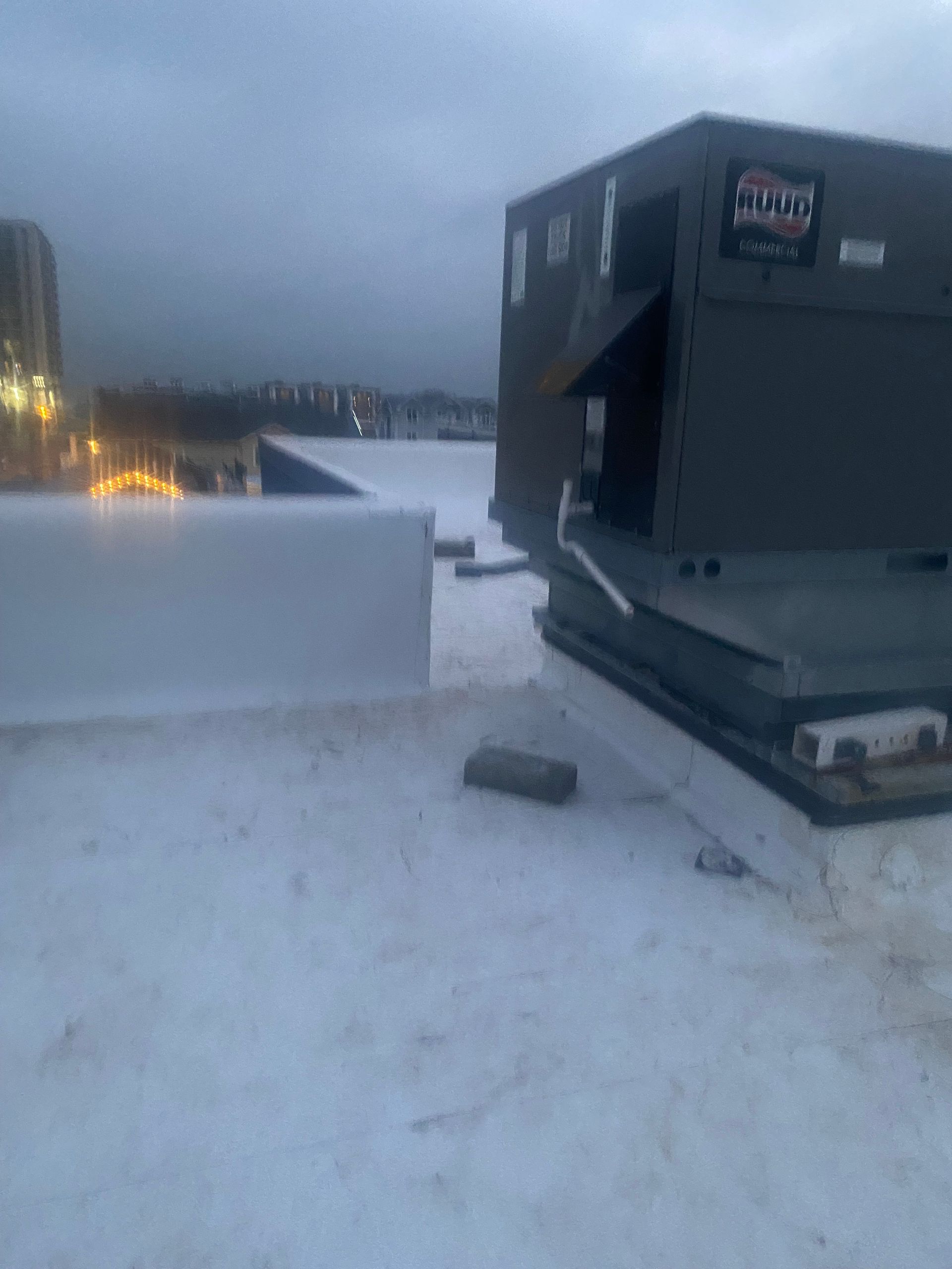 Rooftop view of HVAC unit on a white flat roof. Building and overcast sky in background.