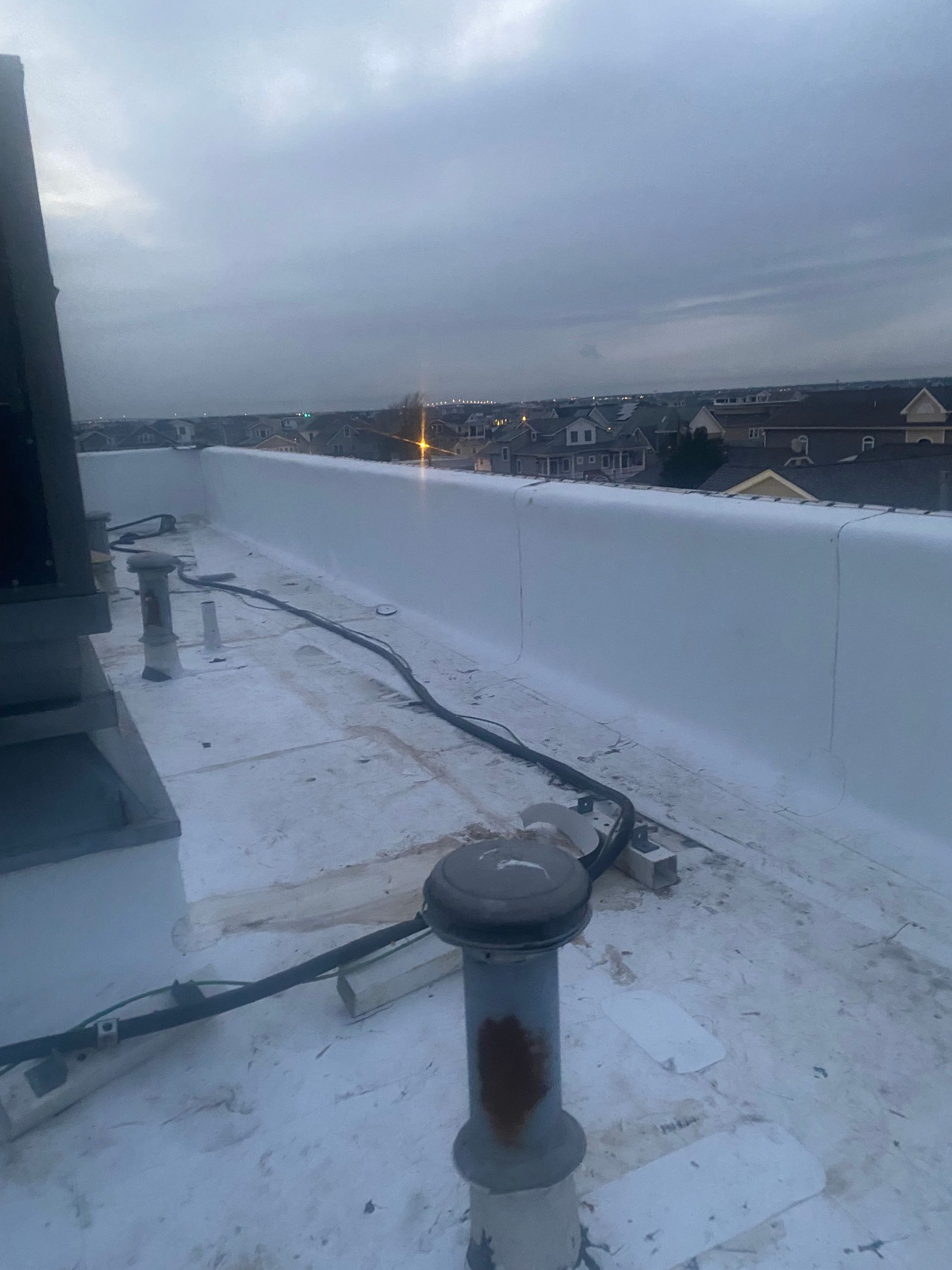 Rooftop with white surface, pipes, and low wall; evening sky in background.