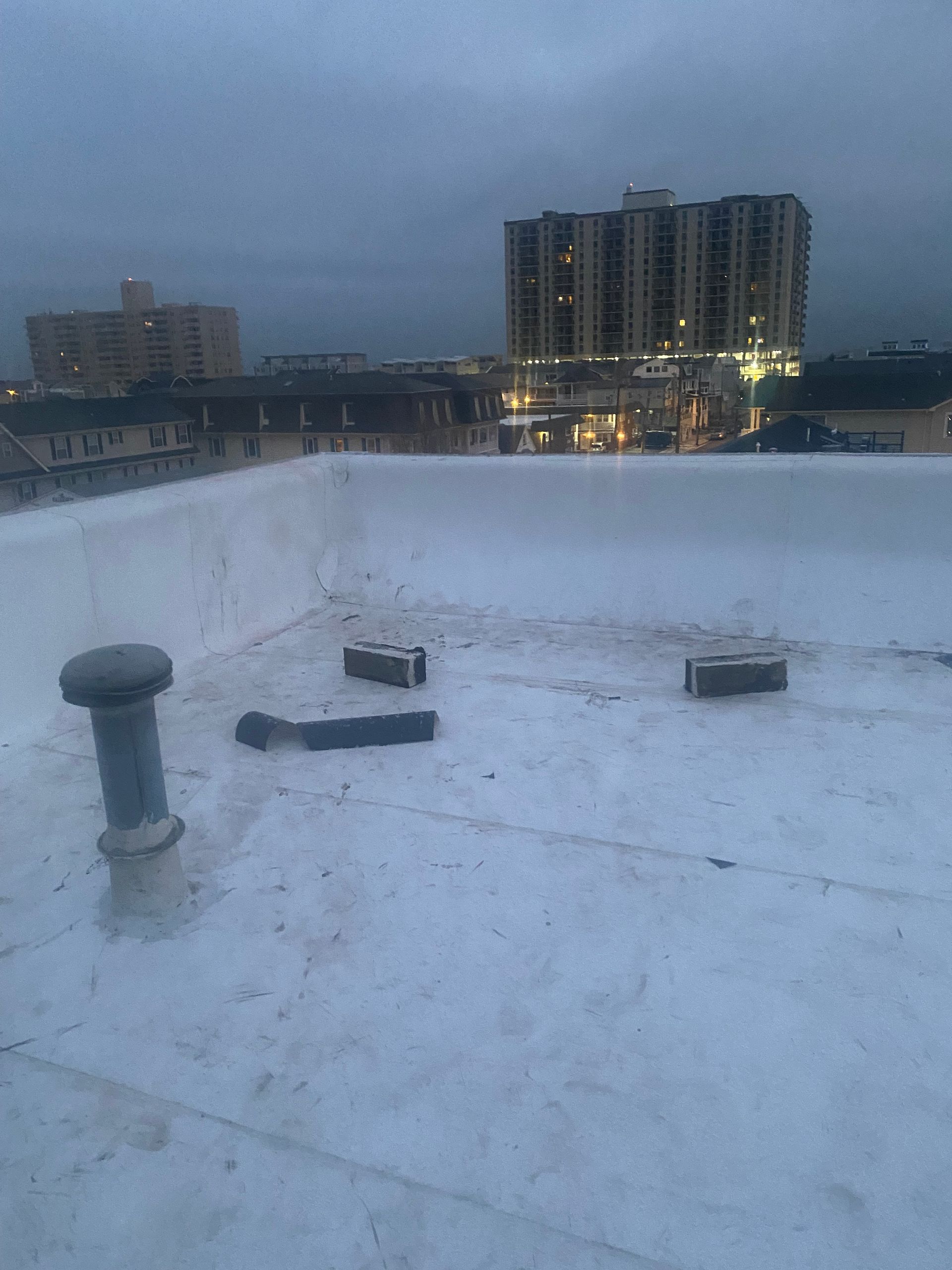 Flat white rooftop with vents, bricks, and a city skyline at dusk.