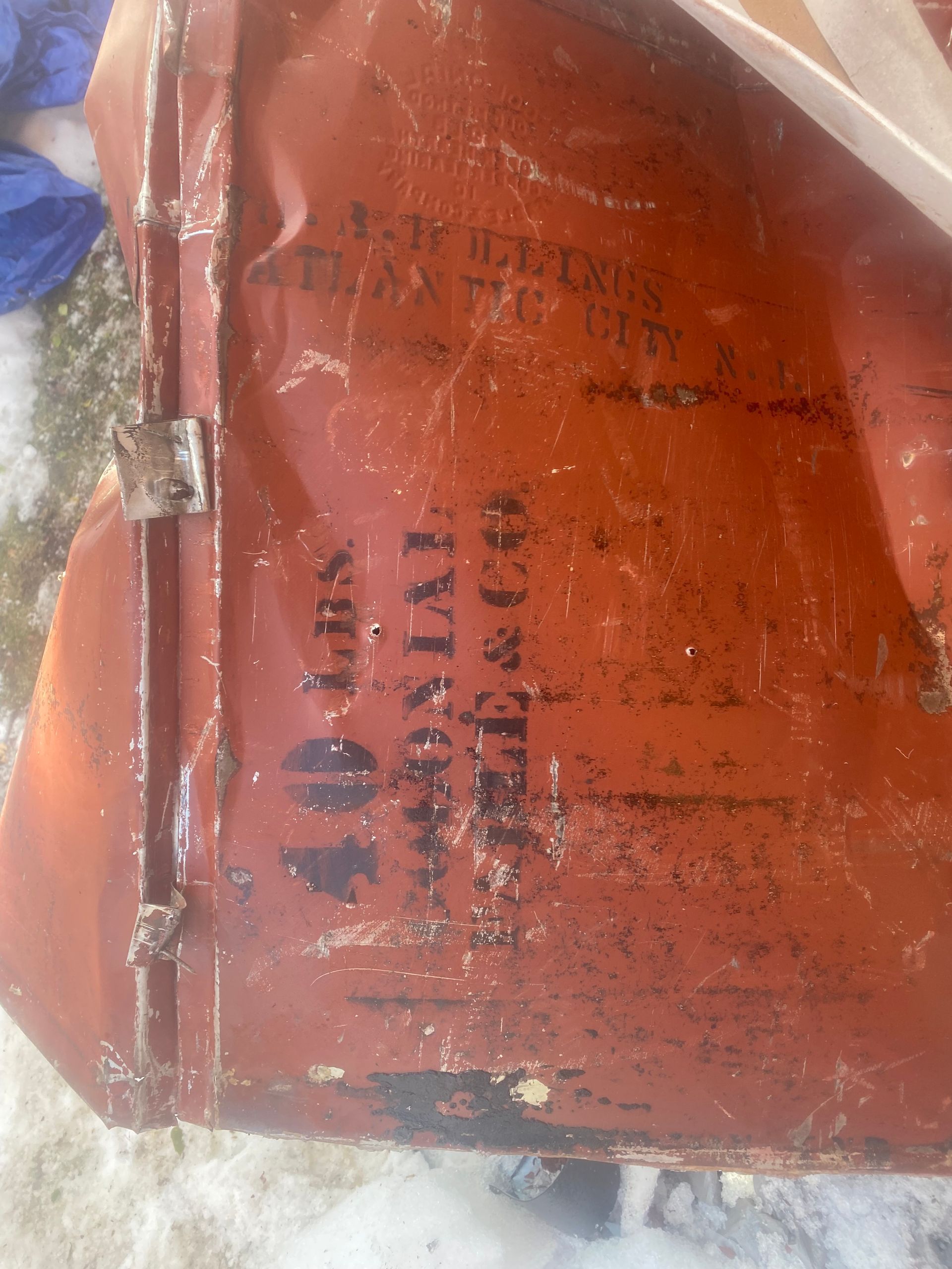 Red-orange metal surface with black stenciled text, partly obscured and worn.