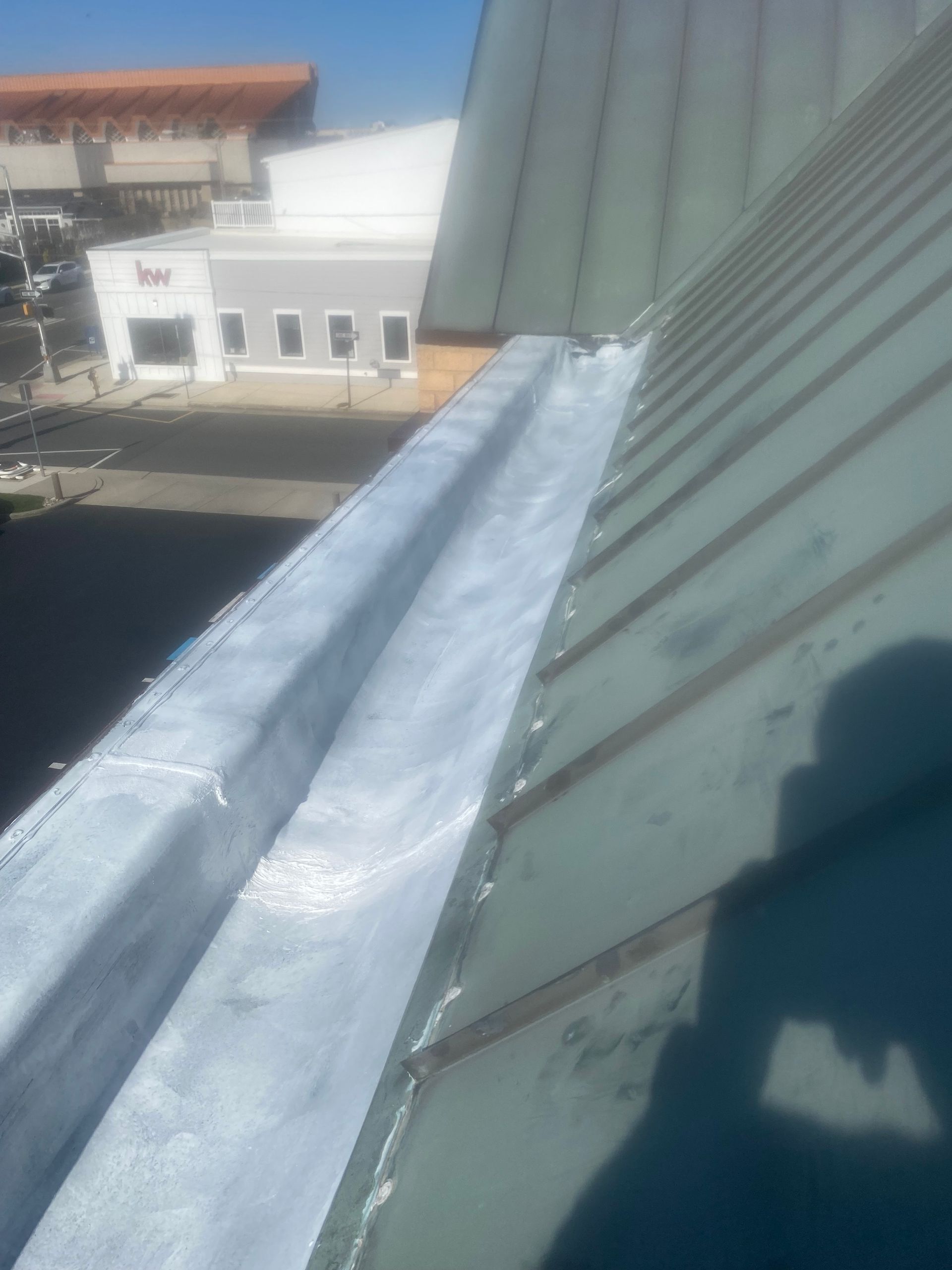 Metal roof with a long silver strip and shadow, viewed from above near buildings