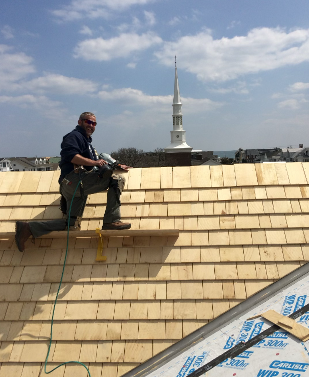 A man is sitting on a wooden roof with a clock tower in the background