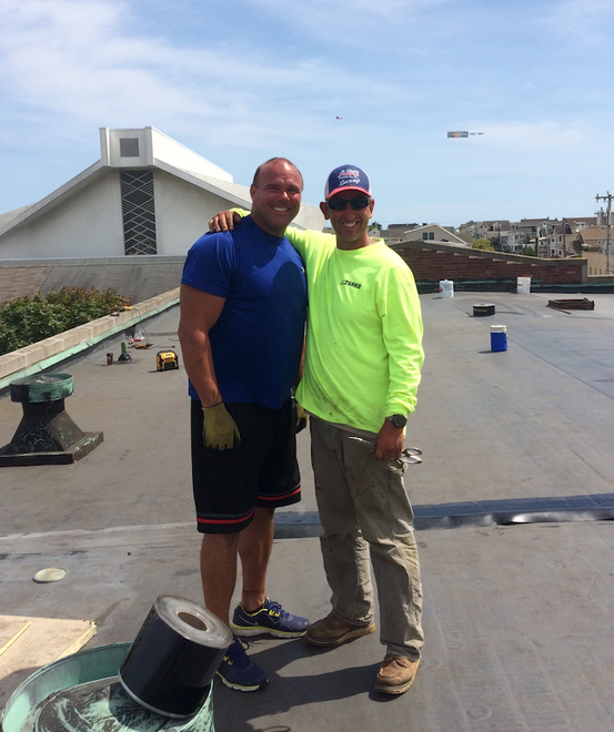 Two men are posing for a picture on a roof