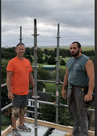 Two men are standing next to each other on top of a scaffolding.