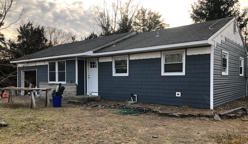 A house with a blue siding and white trim is sitting on top of a dirt field.