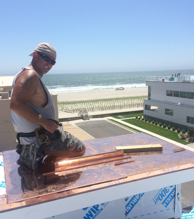 A man is kneeling on a roof with a view of the ocean