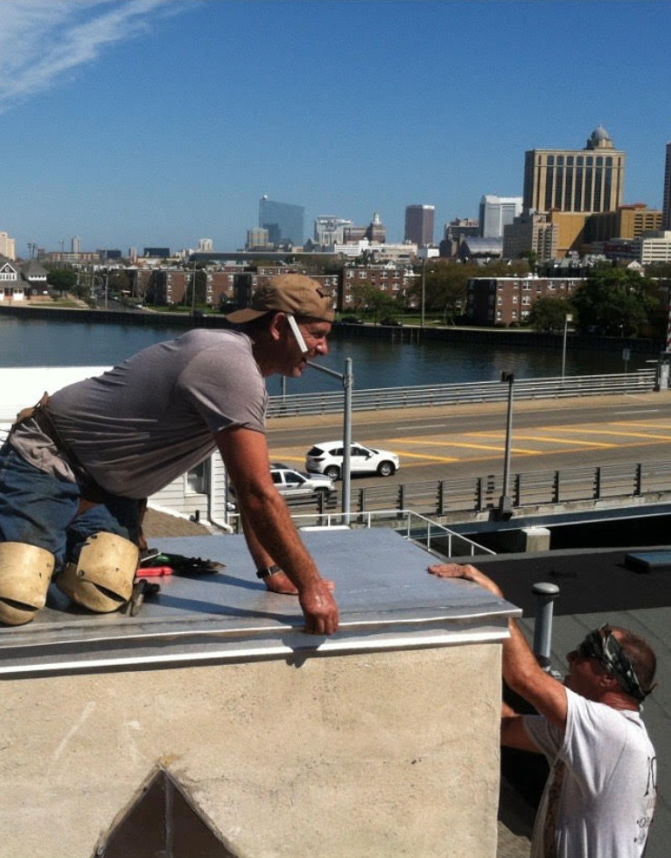 Two men are working on a roof with a city in the background