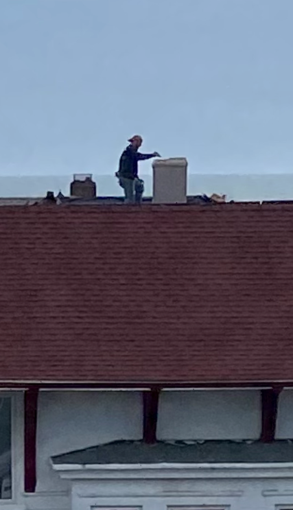 A man is standing on top of a roof working on a chimney.