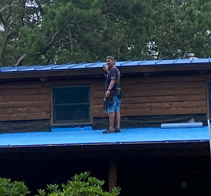 A man is standing on the roof of a log cabin.