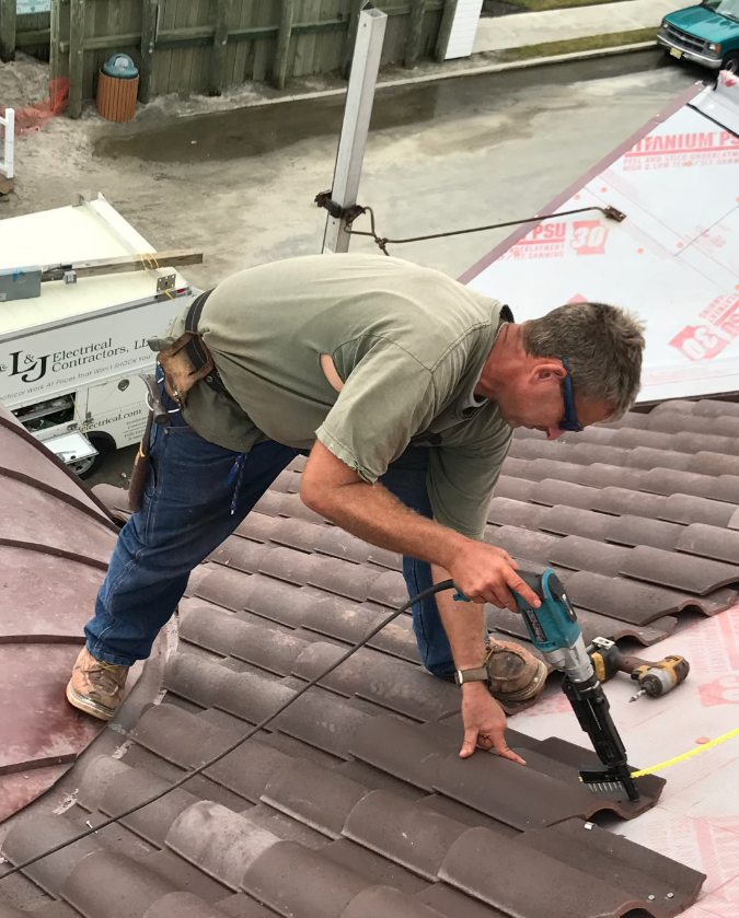 A man is working on a roof with a drill.
