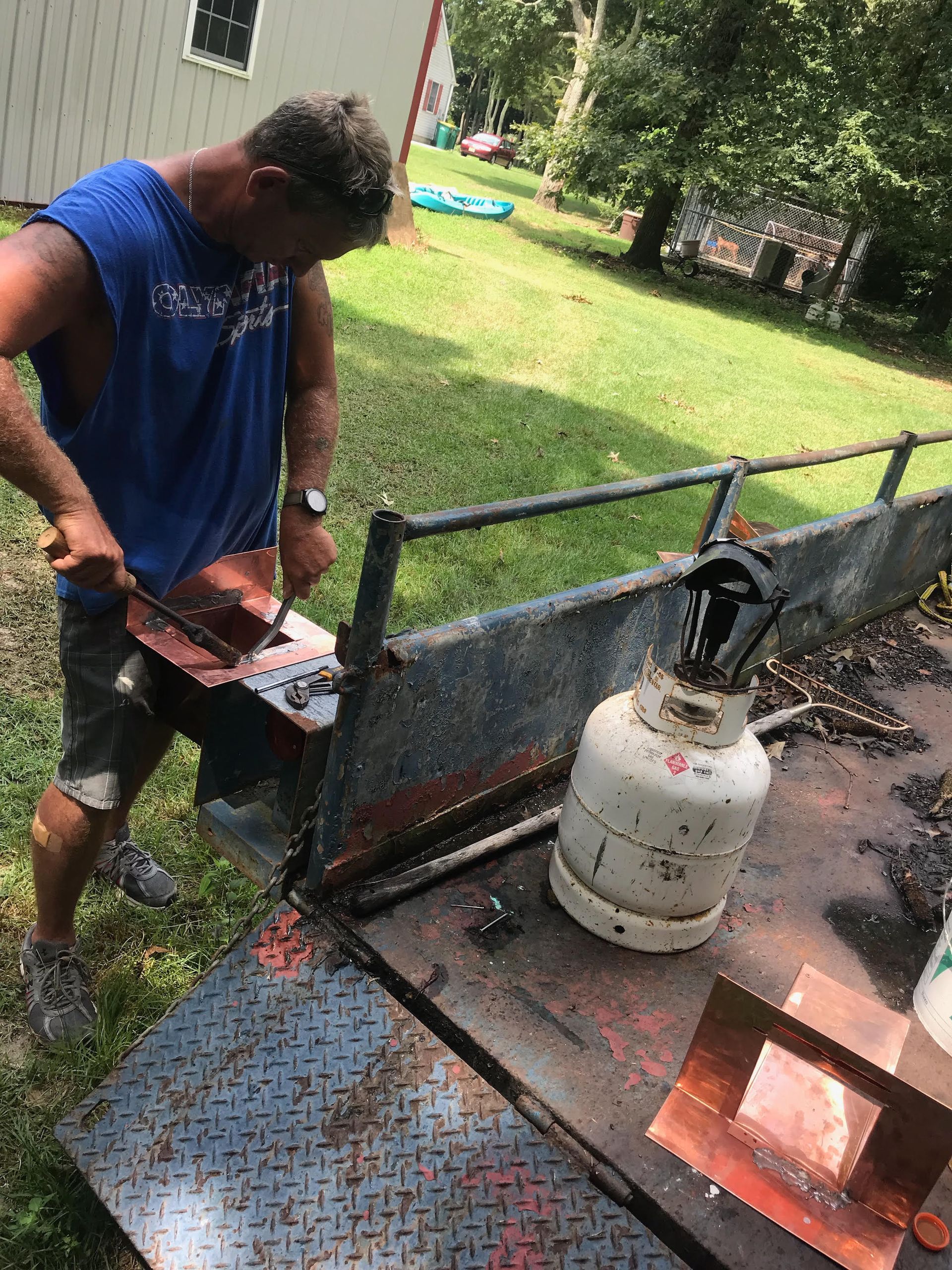 A man is working on a piece of metal next to a propane cylinder.