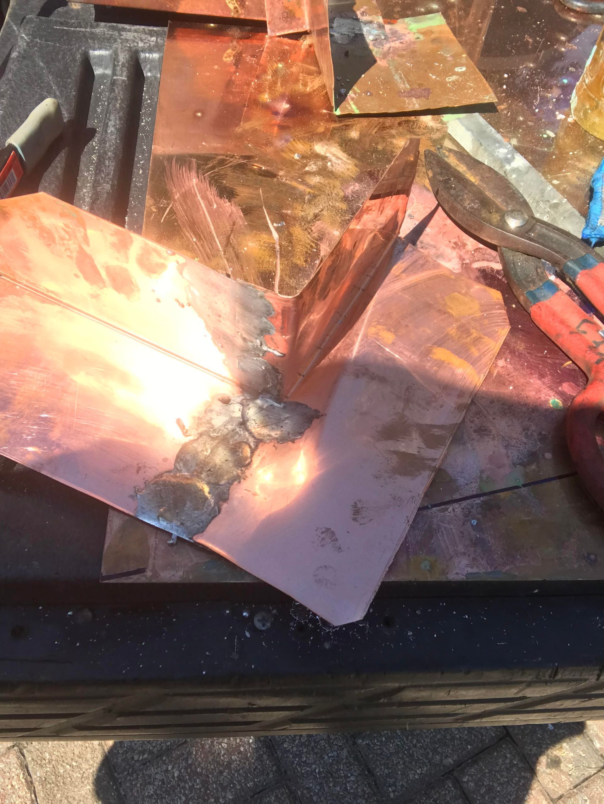 A piece of copper is laying on a table next to a pair of scissors.