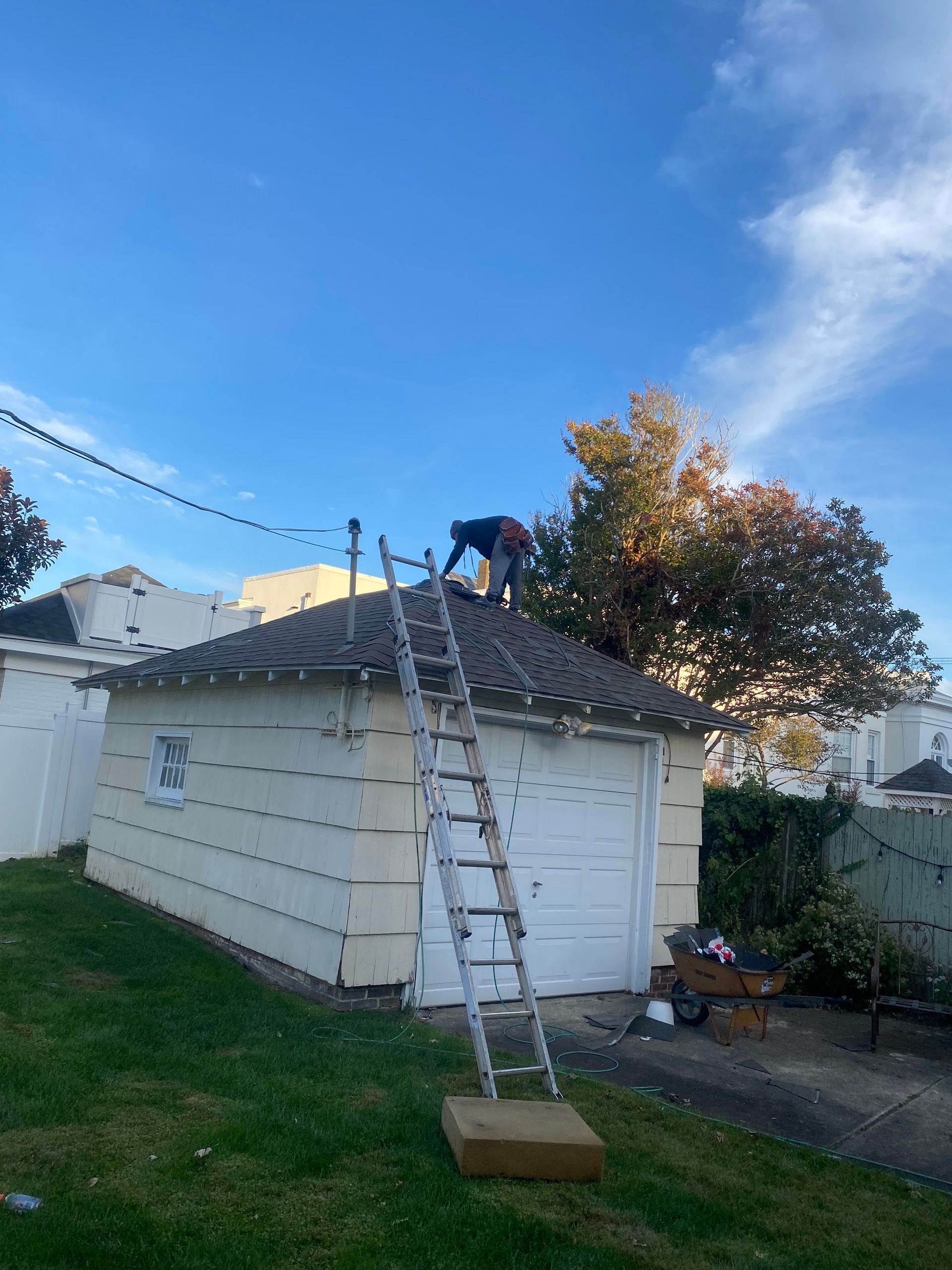 A man is working on the roof of a garage with a ladder.