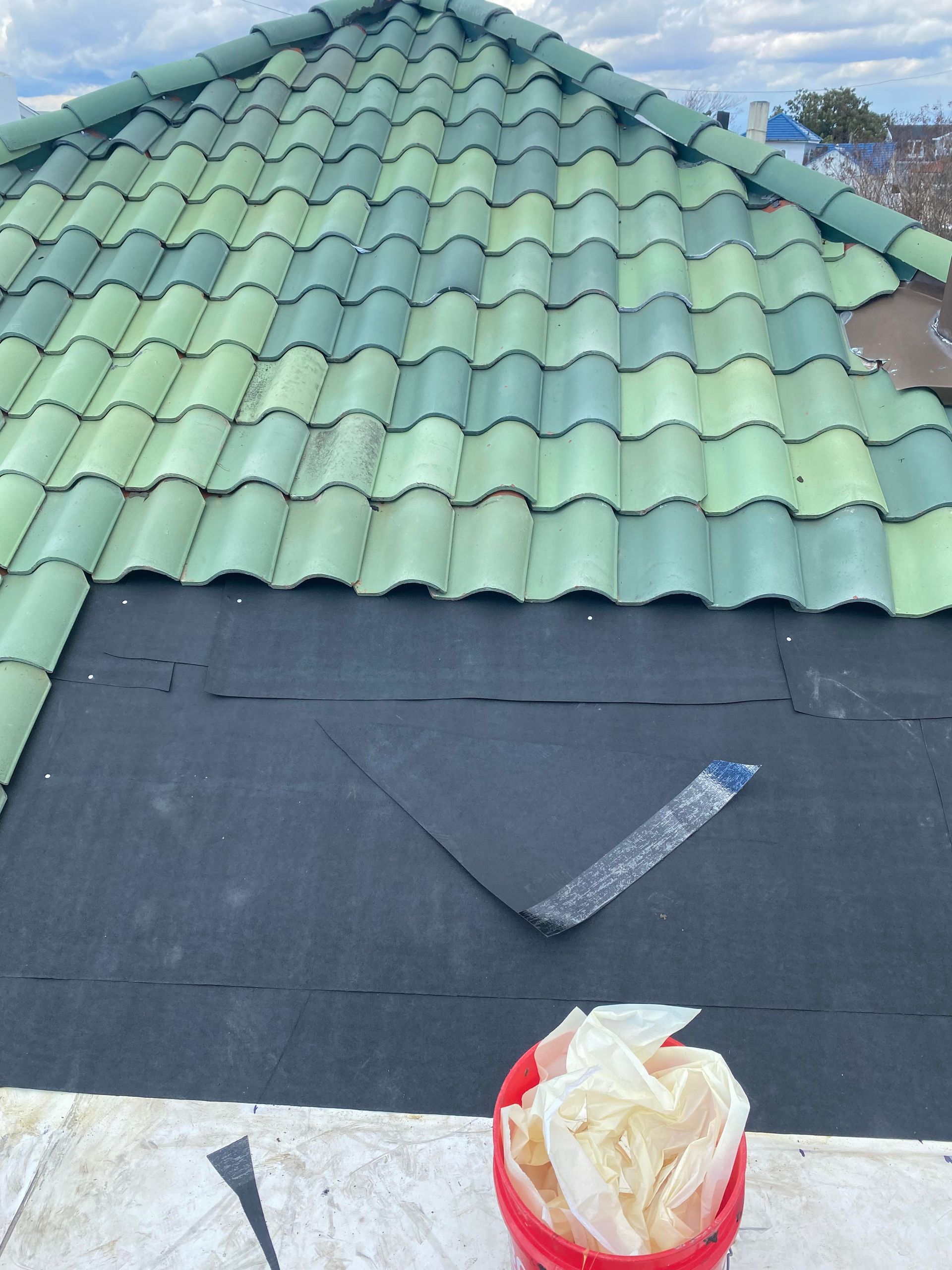 A green tiled roof with a red bucket of shingles on top of it