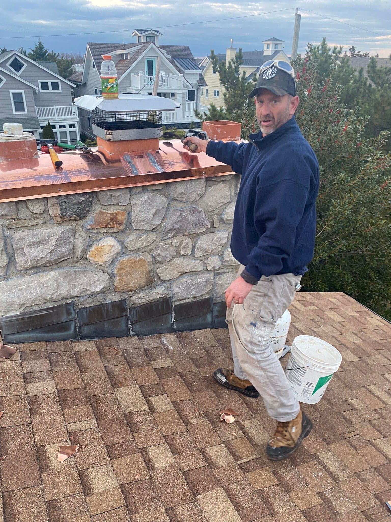 A man is standing on top of a roof holding a bucket.