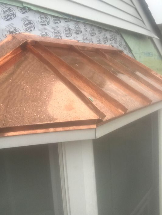 Copper roof over a small porch beside a white house exterior.