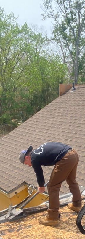 A man is bending over to remove shingles from a roof.