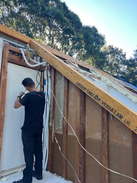 Construction worker installing electrical wiring on a building exterior. Wooden framing, white conduit, and open wall.